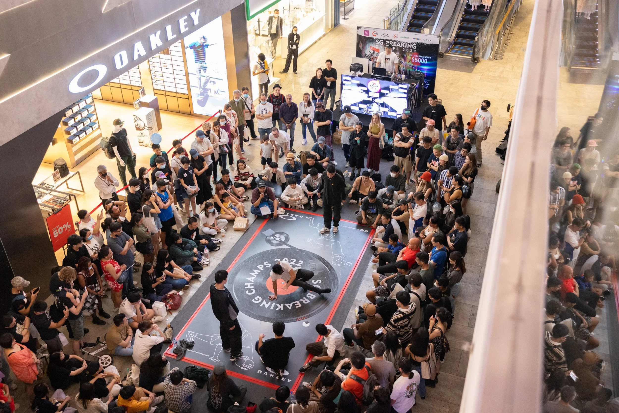  Elevated wide-angle photograph of a breakdancer executing intricate groundwork transitions on stage. 