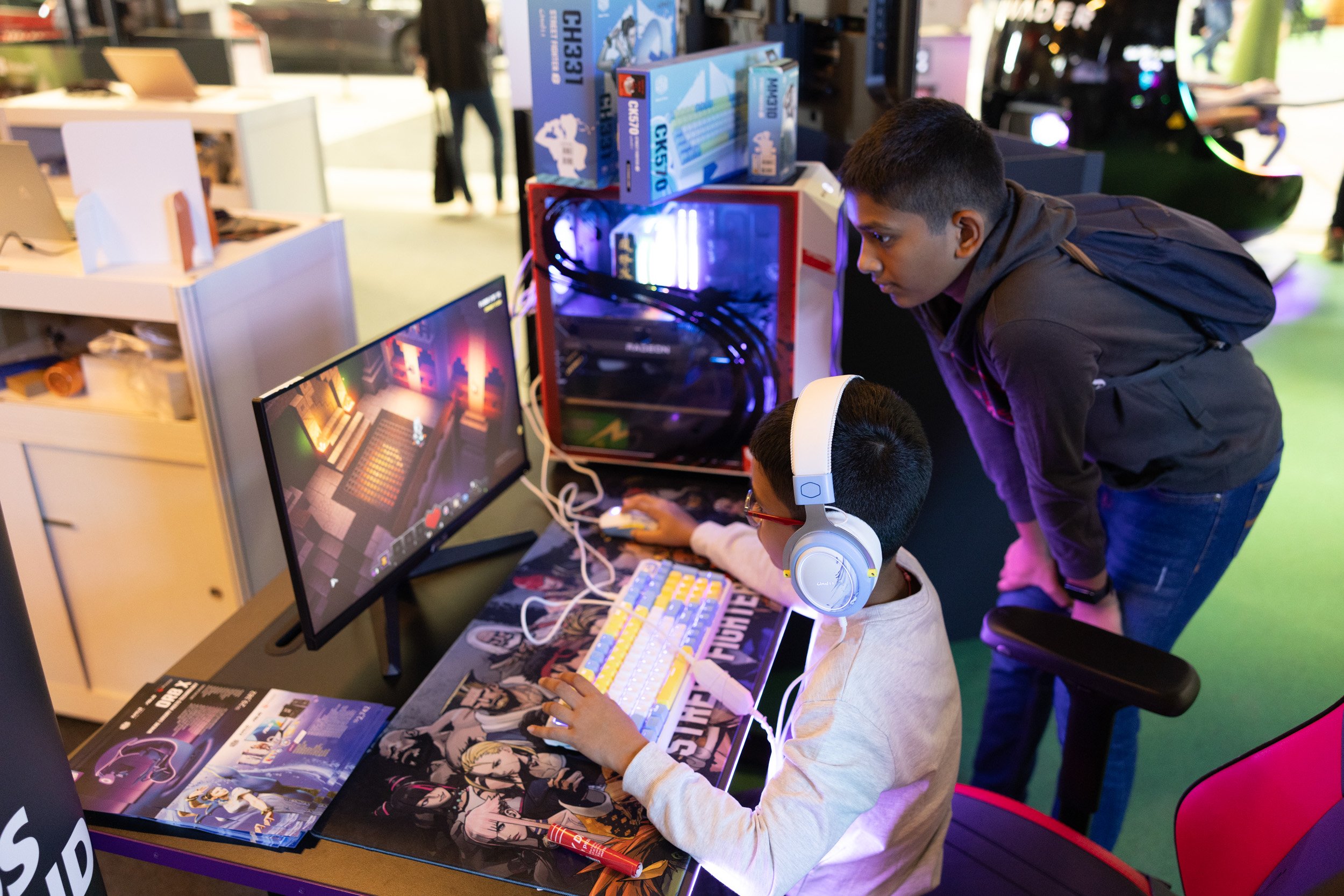  Young attendees participating in a PC gaming challenge with headsets at the AMD experience booth. 