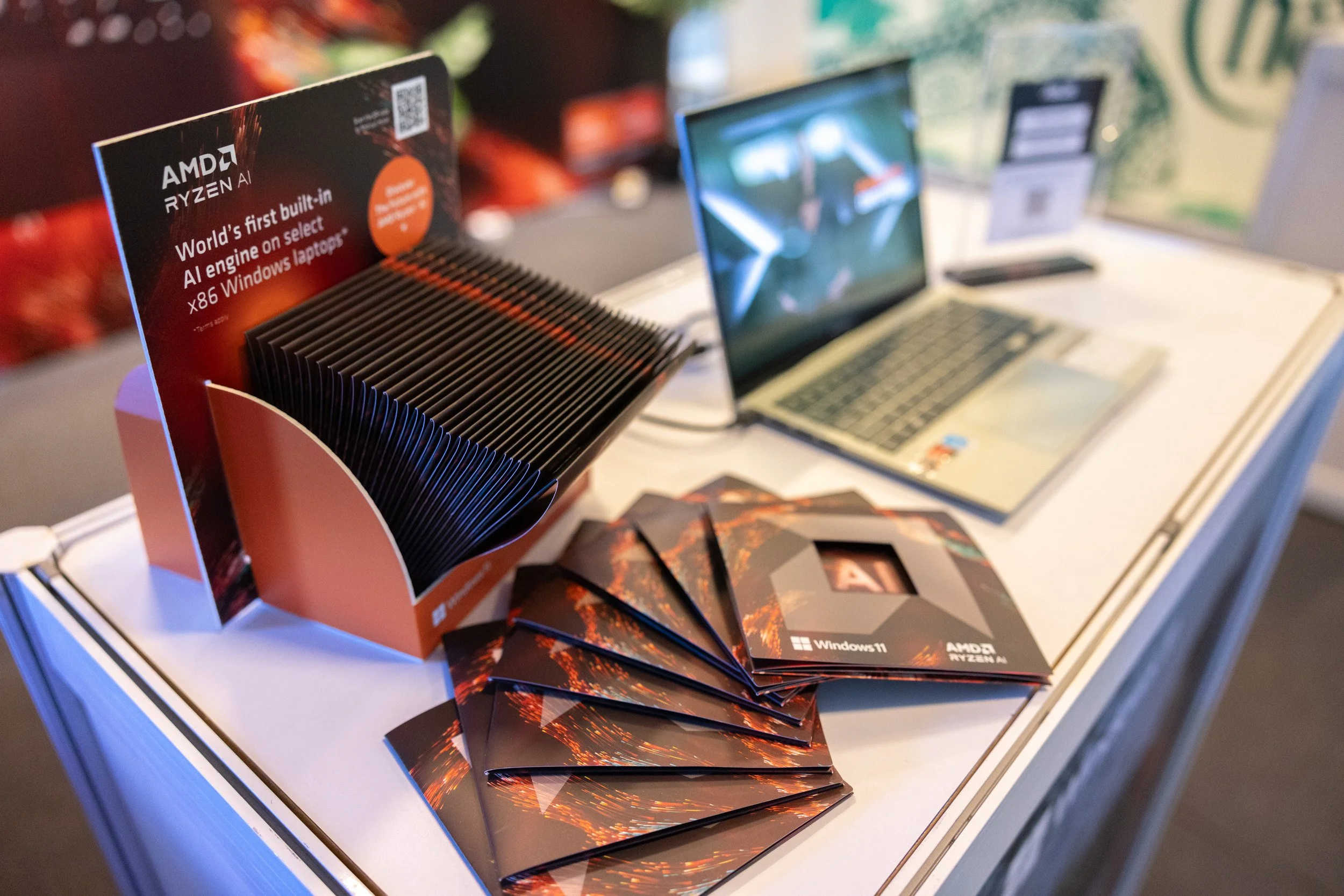  Educational AMD Ryzen AI brochures neatly arranged alongside a demo laptop on an event table. 
