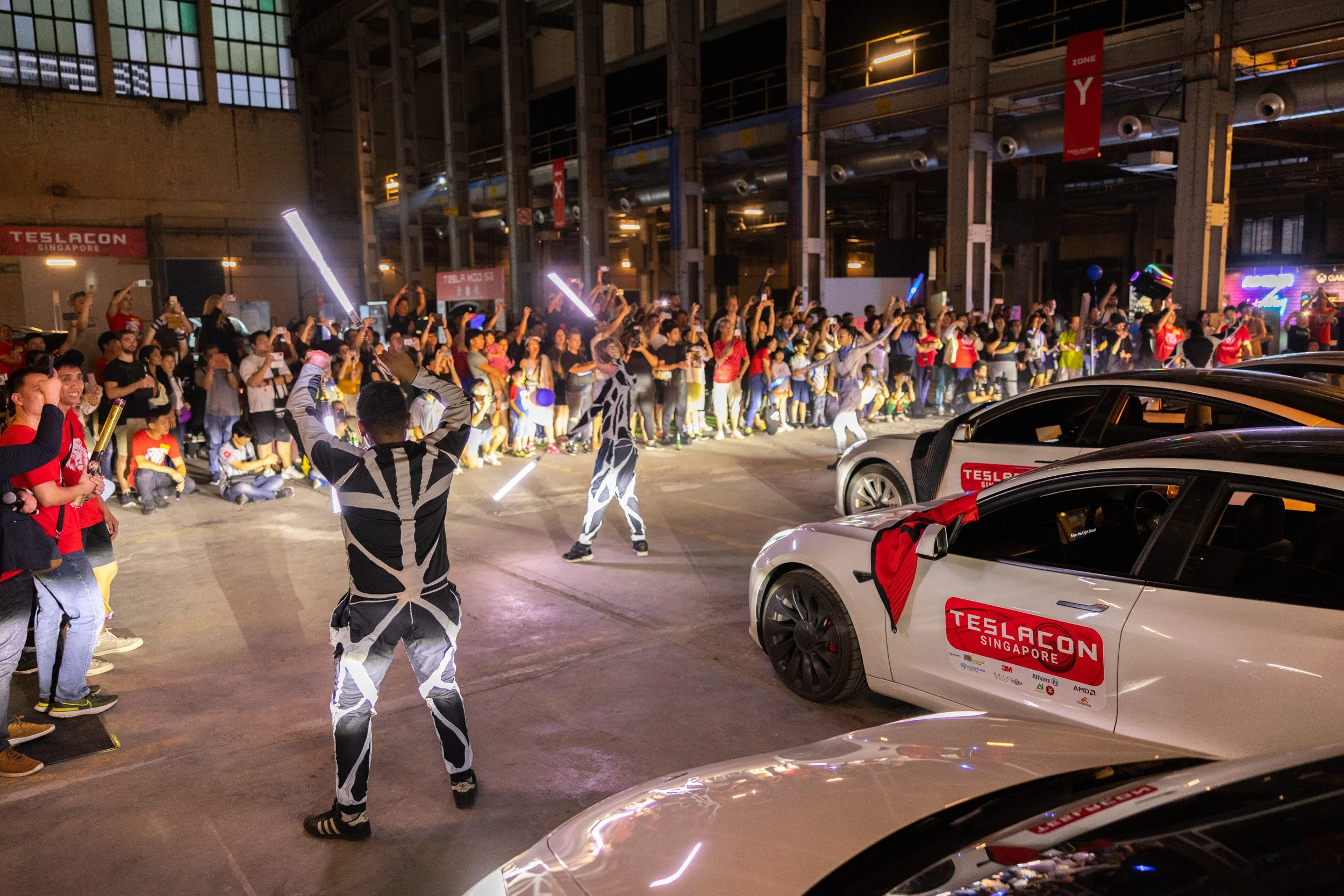  Wide perspective of live entertainment and dance performances taking place in front of featured Tesla vehicles. 