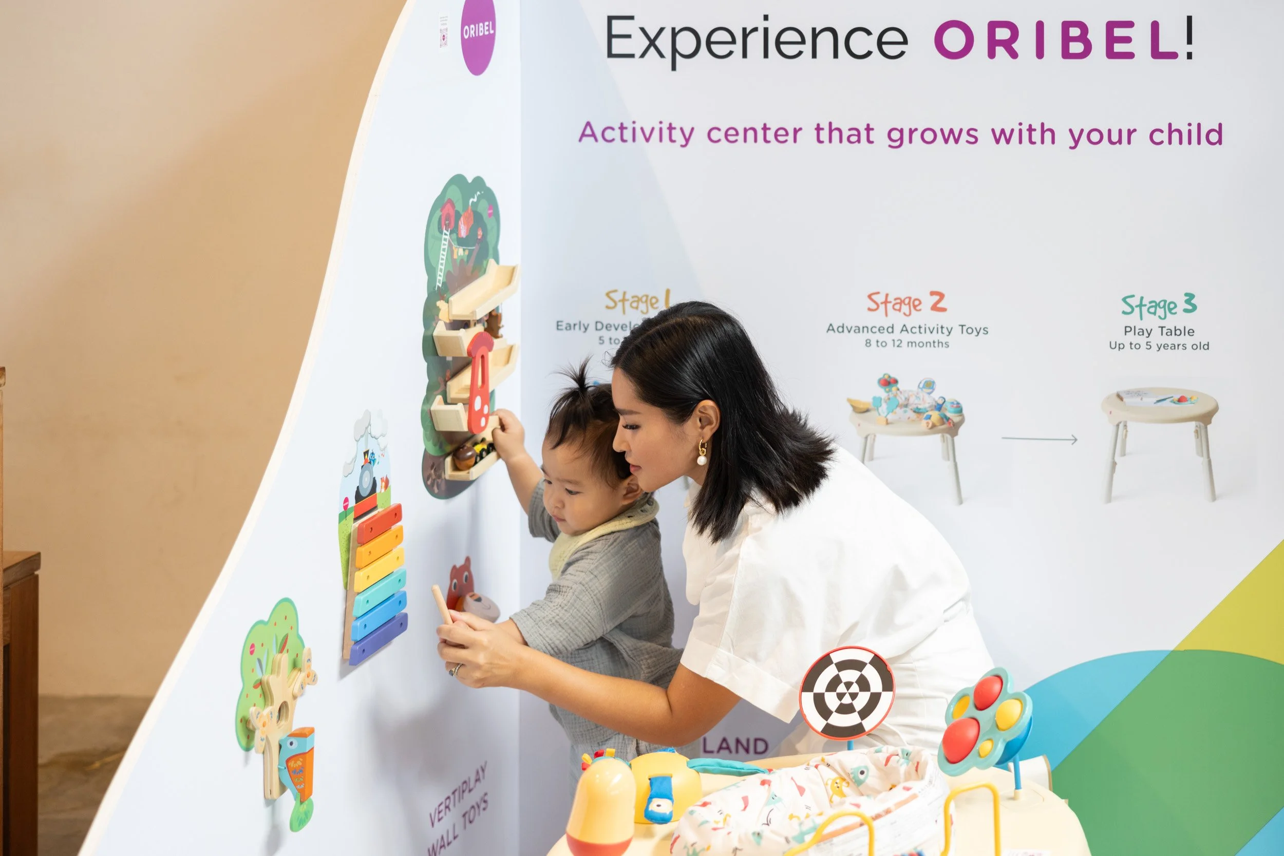  Mother and child playing with Oribel VertiPlay wall toys beside brand product signage. 