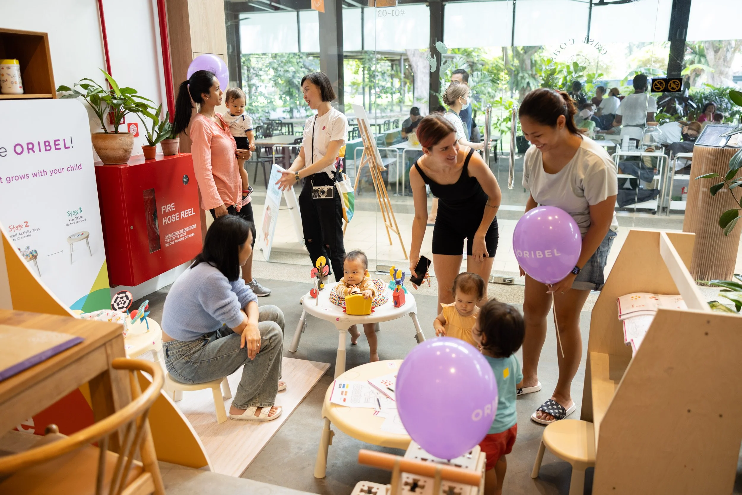  Mid-range photograph of parents exploring Oribel baby gear in the venue play zone. 