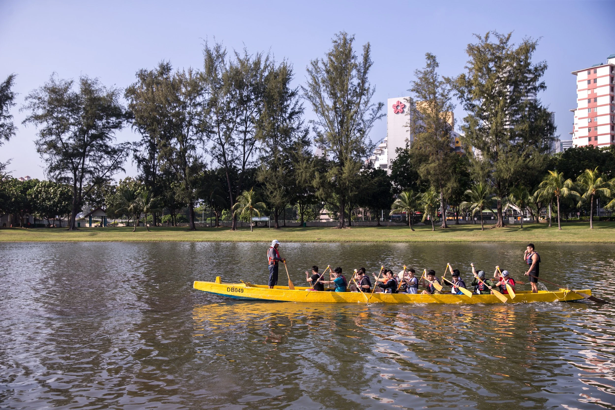  Distance profile shot of a dragon boat paddling along the lush green riverbanks of Kallang Basin. 