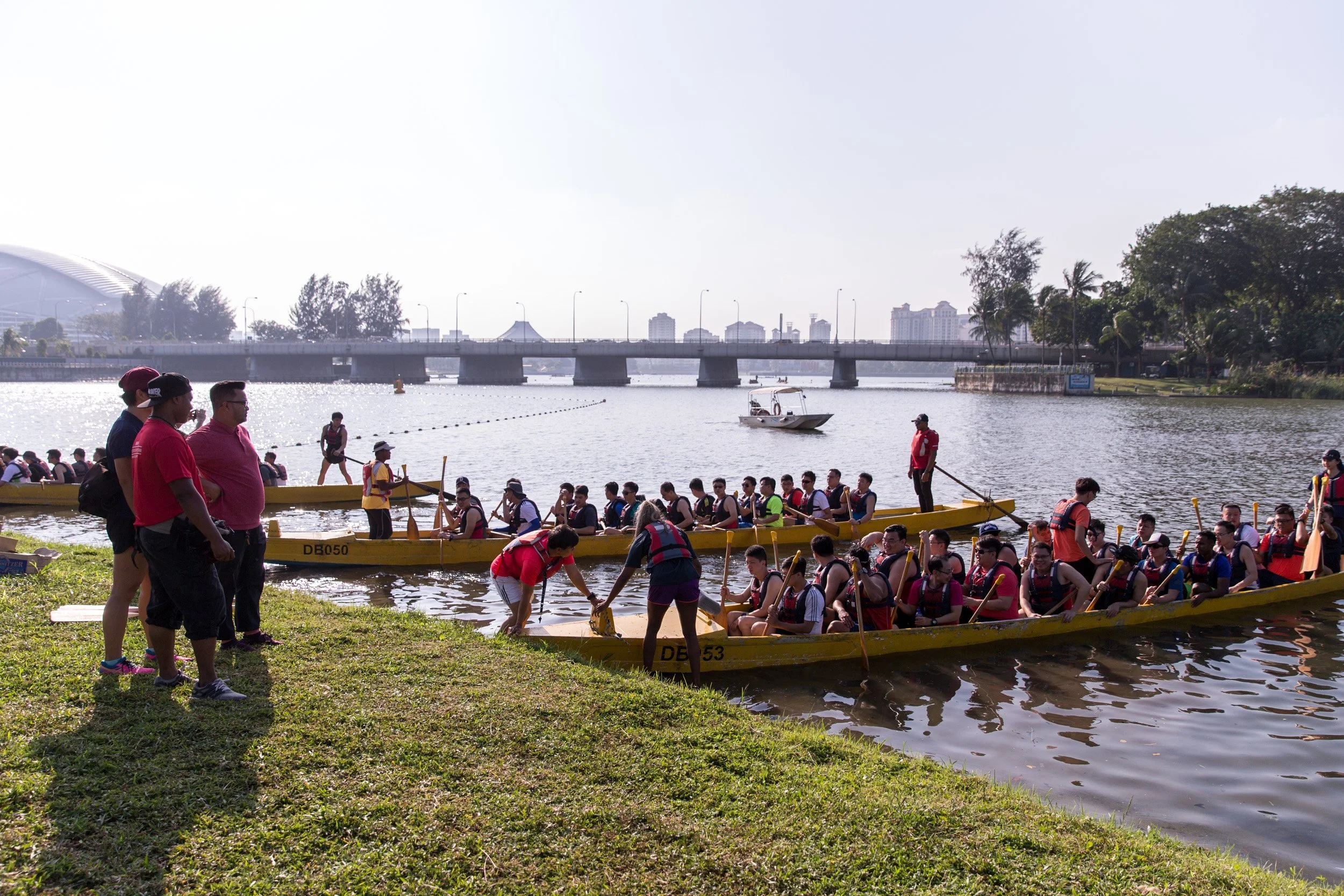  Wide-angle view of multiple team dragon boats pushing off from the riverbank during the team-building activity. 