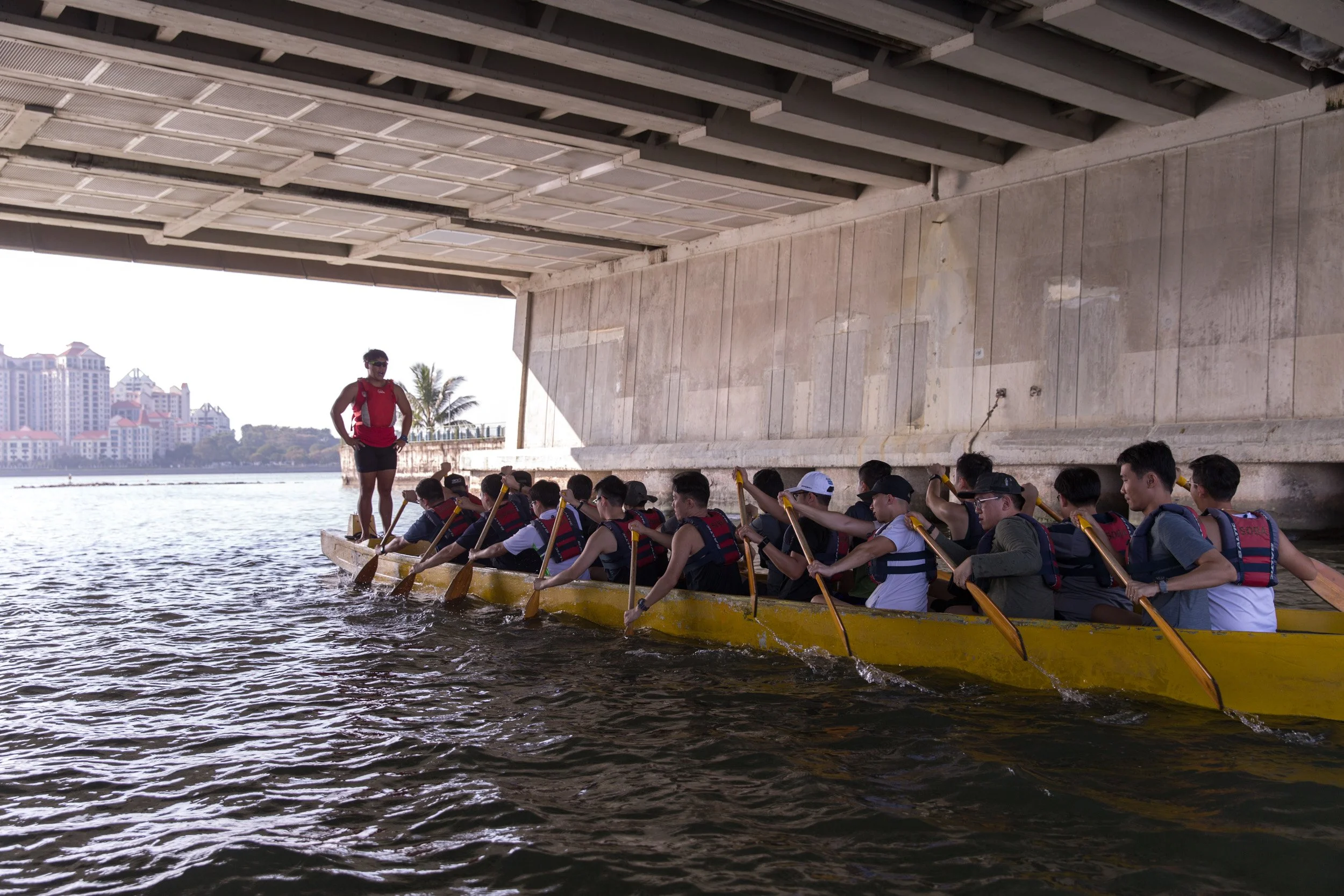 Dragon boat team navigating under a highway bridge overpass during their open-water paddling session. 