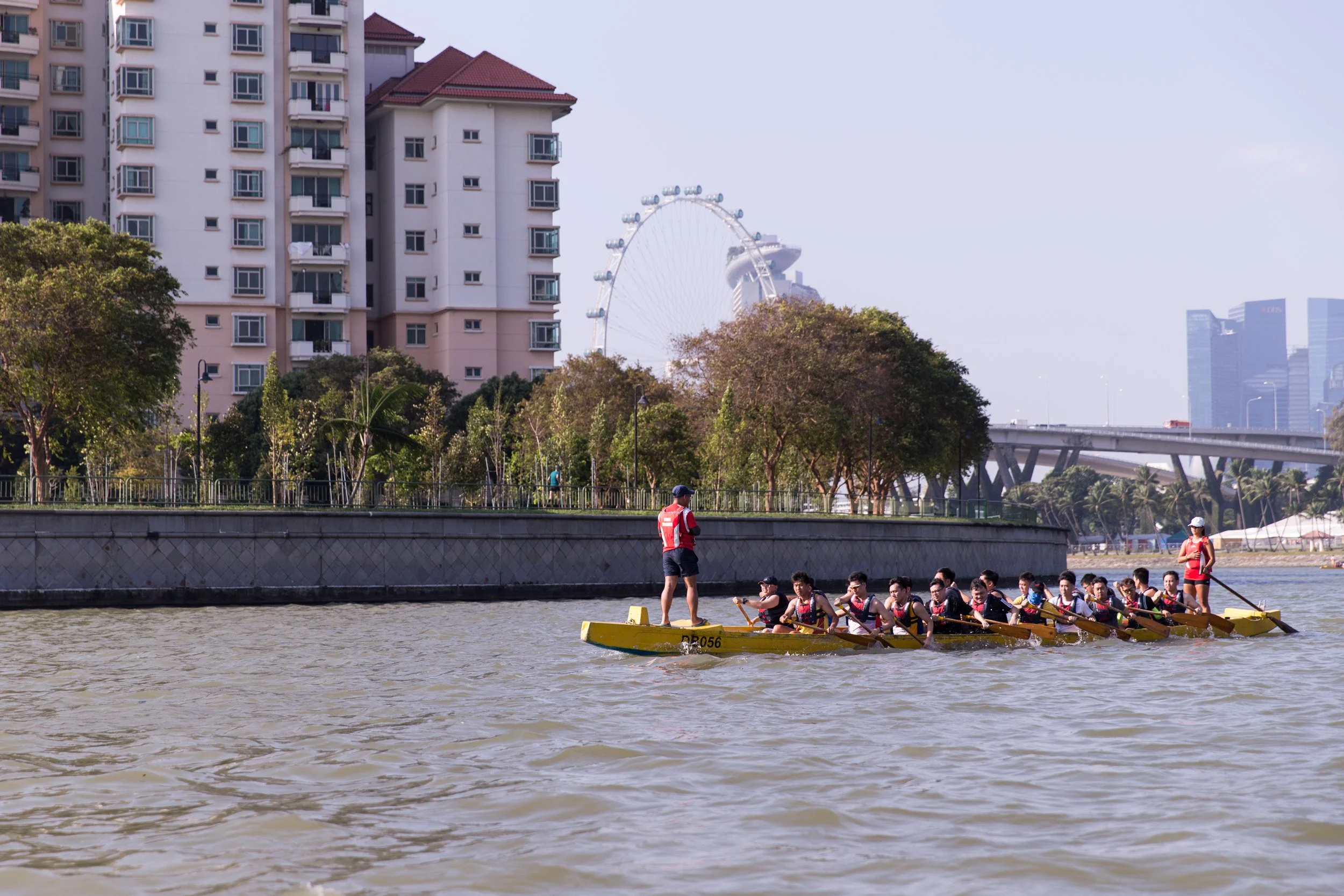  Wide scenic view of a dragon boat crossing Kallang Basin with the iconic Singapore Flyer in the skyline background. 