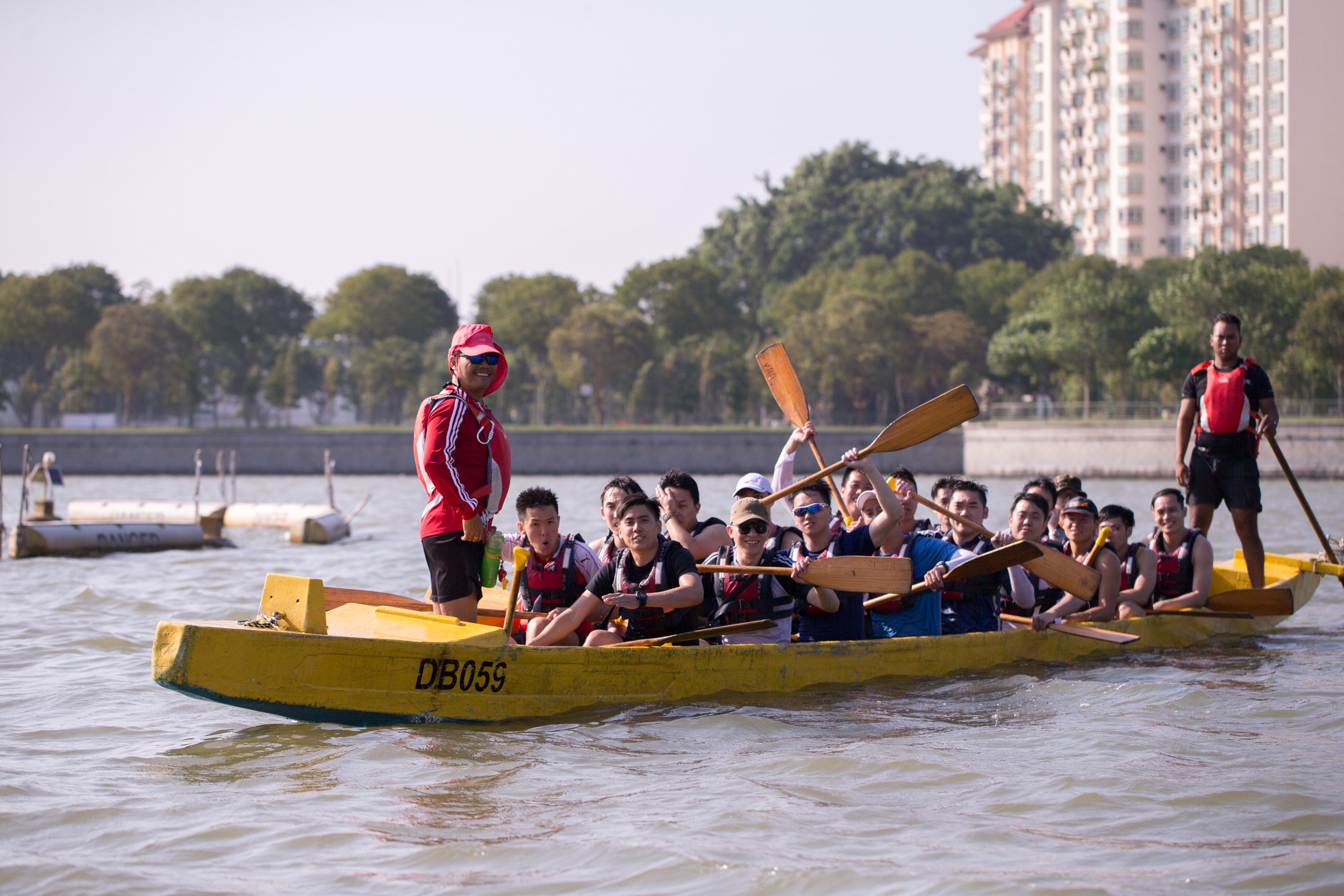  Candid group shot of dragon boat participants holding up paddles and smiling on the water. 