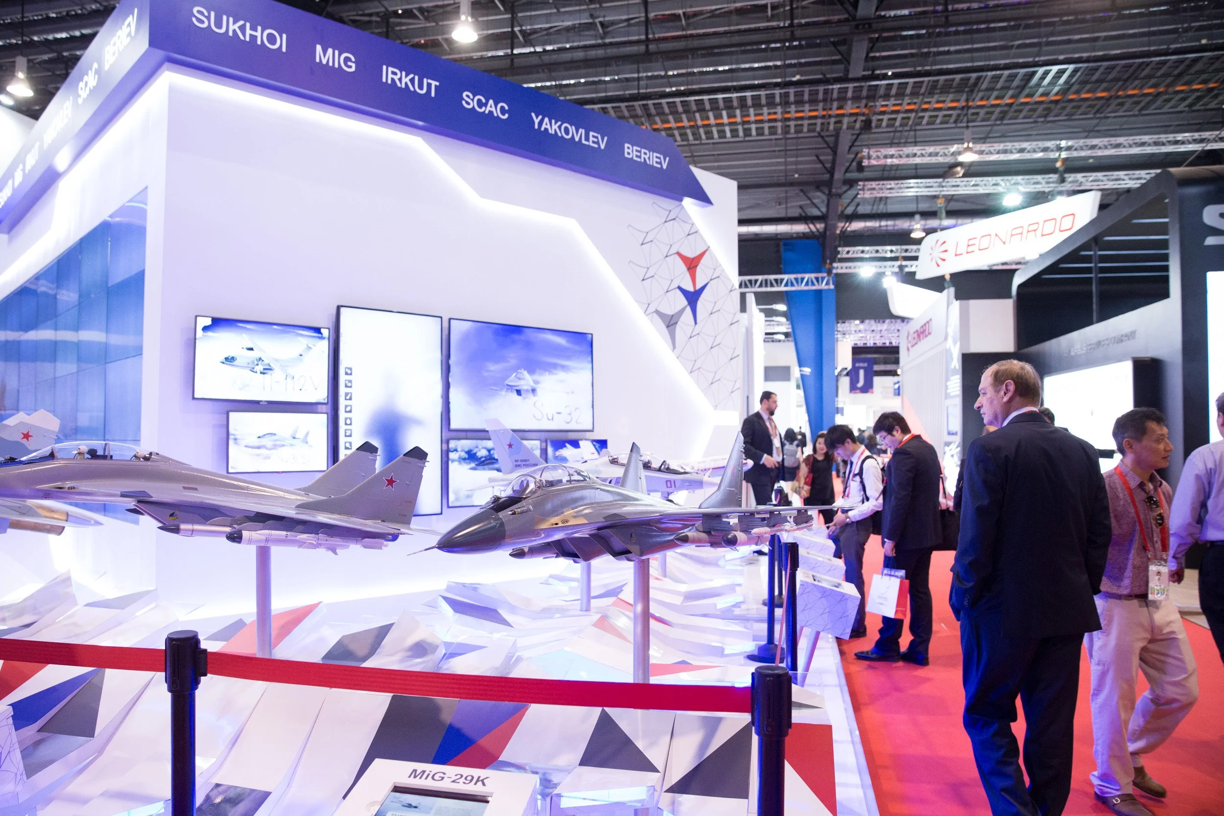  Aviation trade delegate examining miniature airplane models at a defense contractor exhibition stand. 