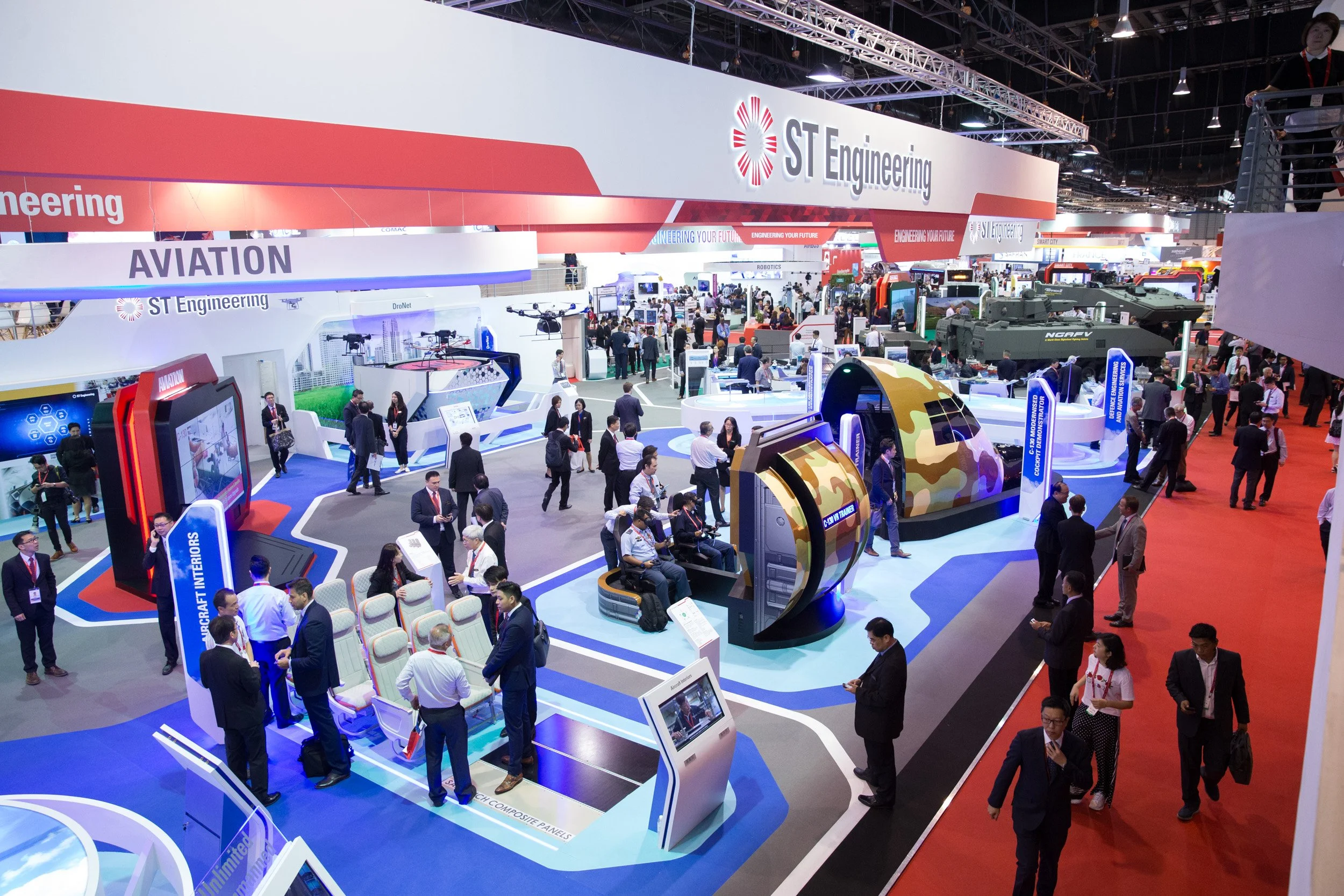  High-angle wide shot of corporate exhibition booths and aerospace industry networking sessions. 