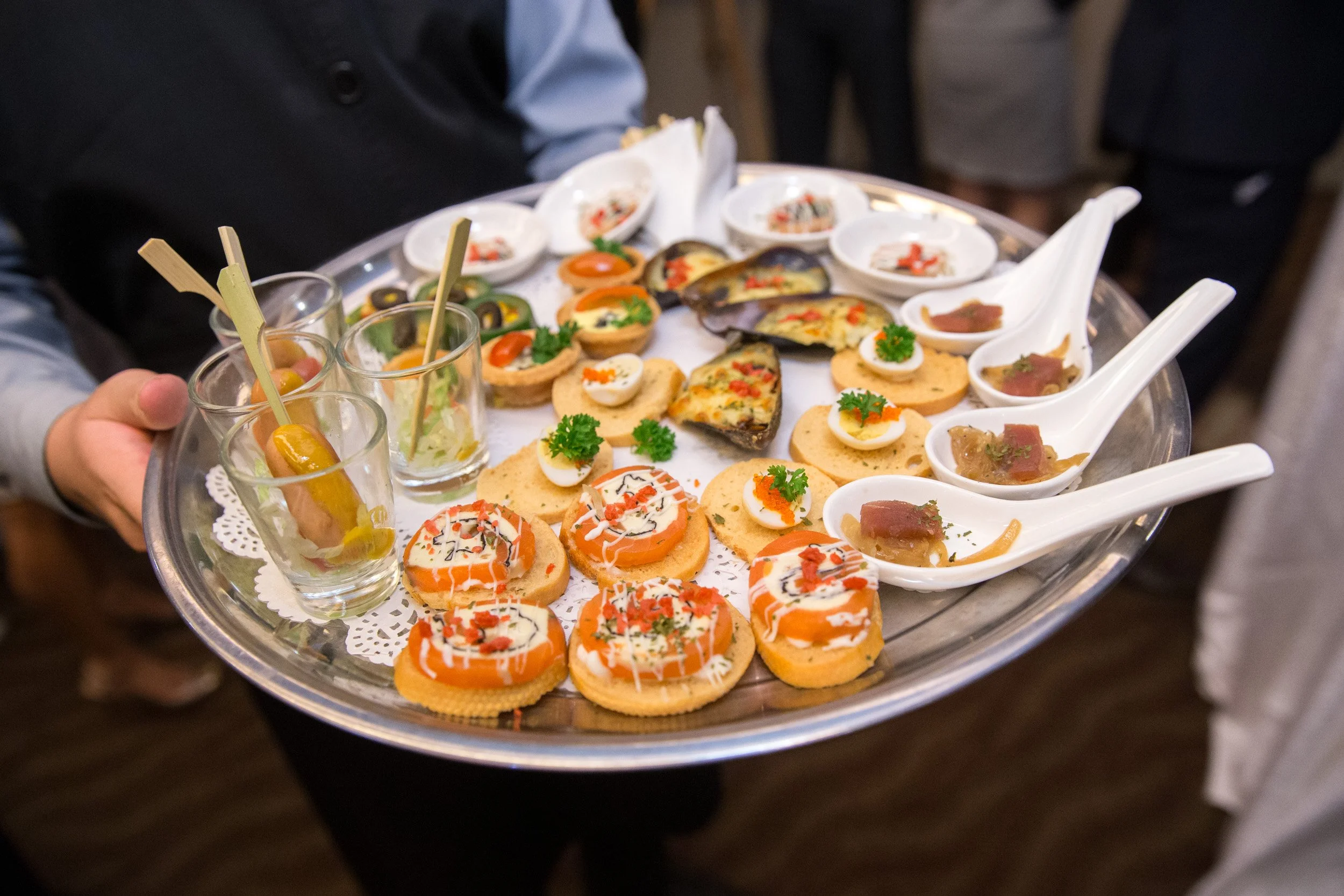  Detail shot of curated gourmet finger food and hors d'oeuvres presented on a tray by service staff. 