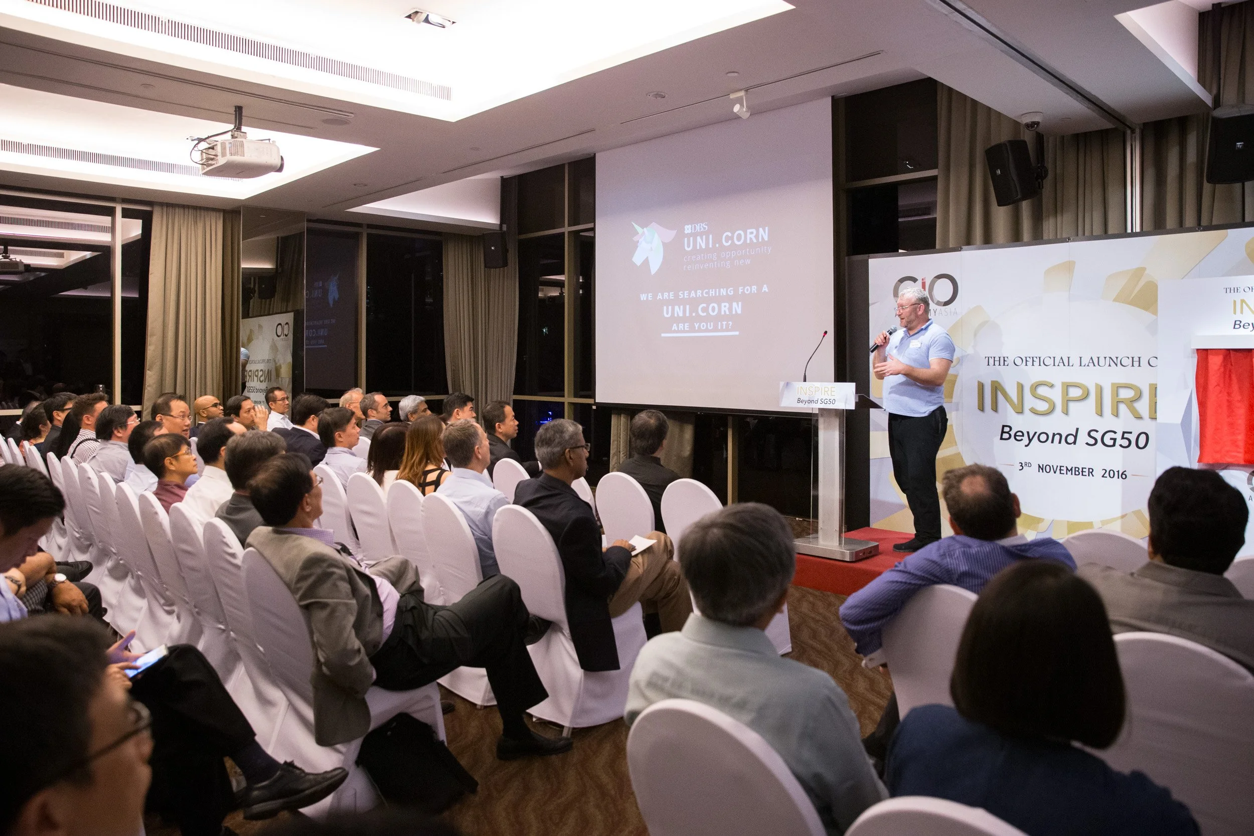  Wide stage view of keynote speaker Neal Cross presenting to technology leaders and executive delegates. 