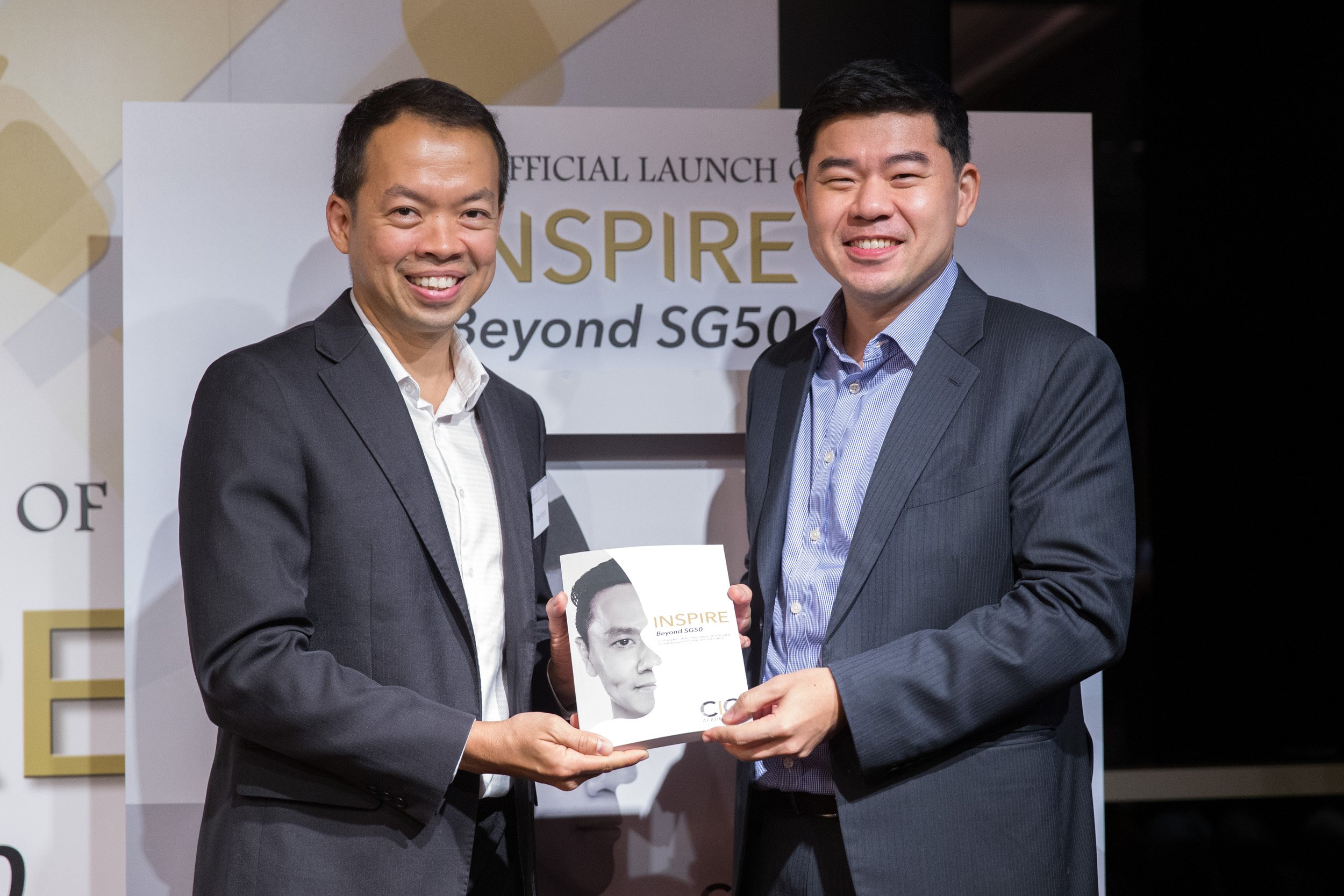  Posed portrait of Guest of Honor Gabriel Lim and Glen Francis holding a copy of "Inspire Beyond SG50" on stage. 