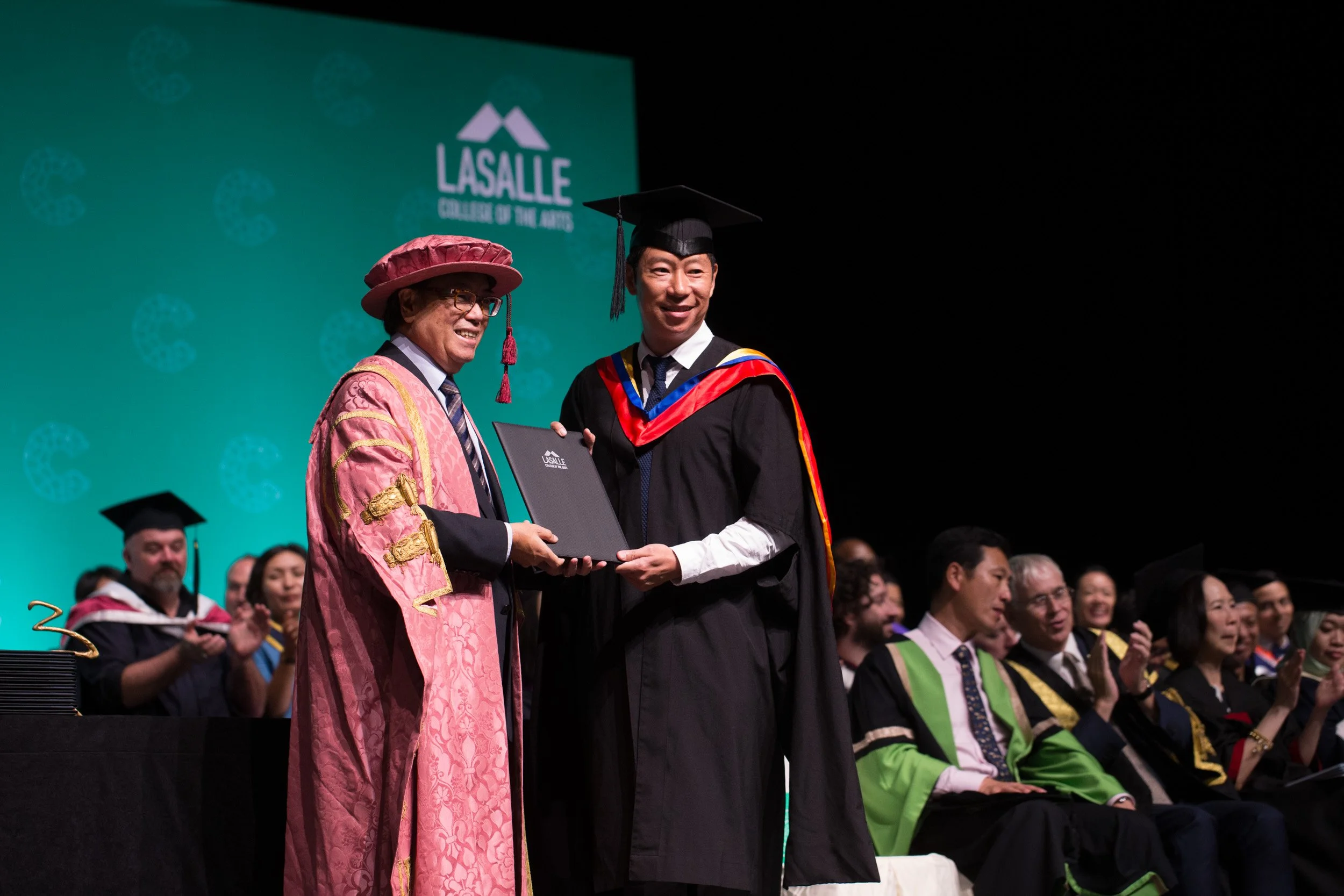  Medium shot of a LASALLE graduate receiving their degree scroll on stage at Singapore EXPO. 