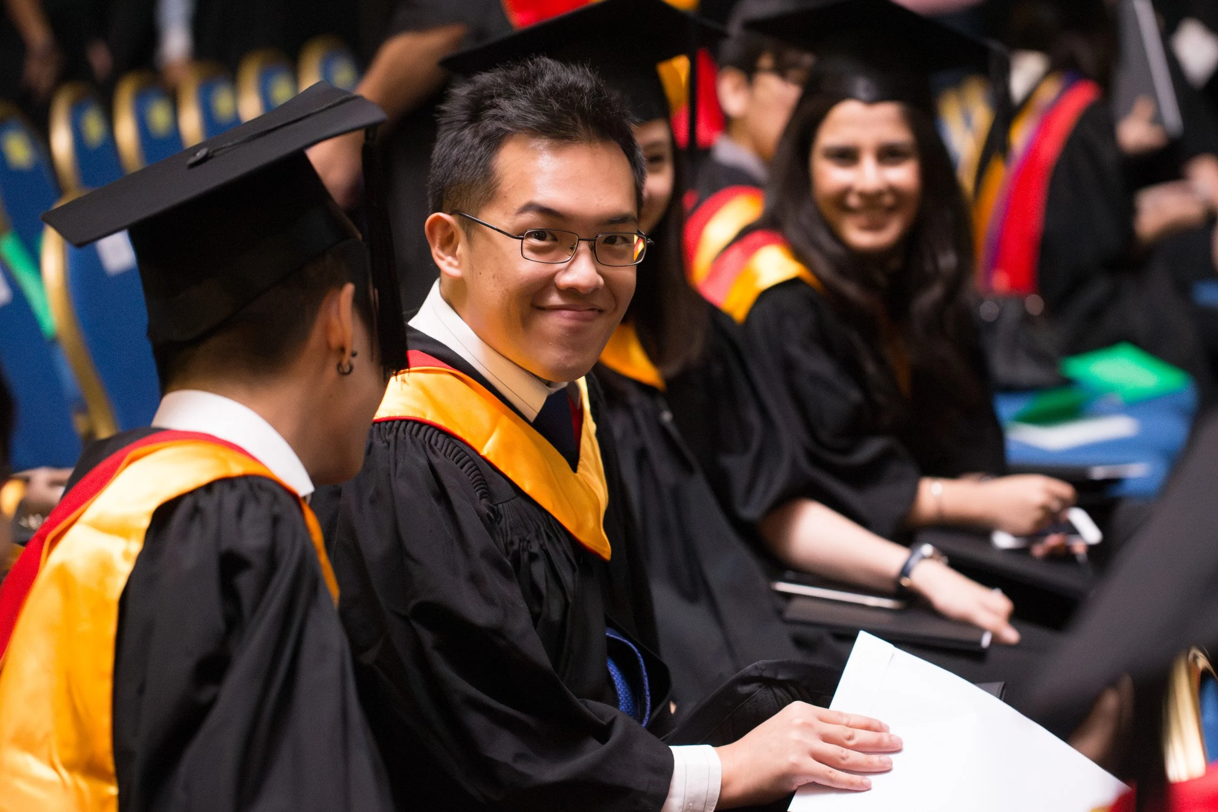  Candid shot of a male graduate engaging with the photographer during the post-ceremony celebrations. 