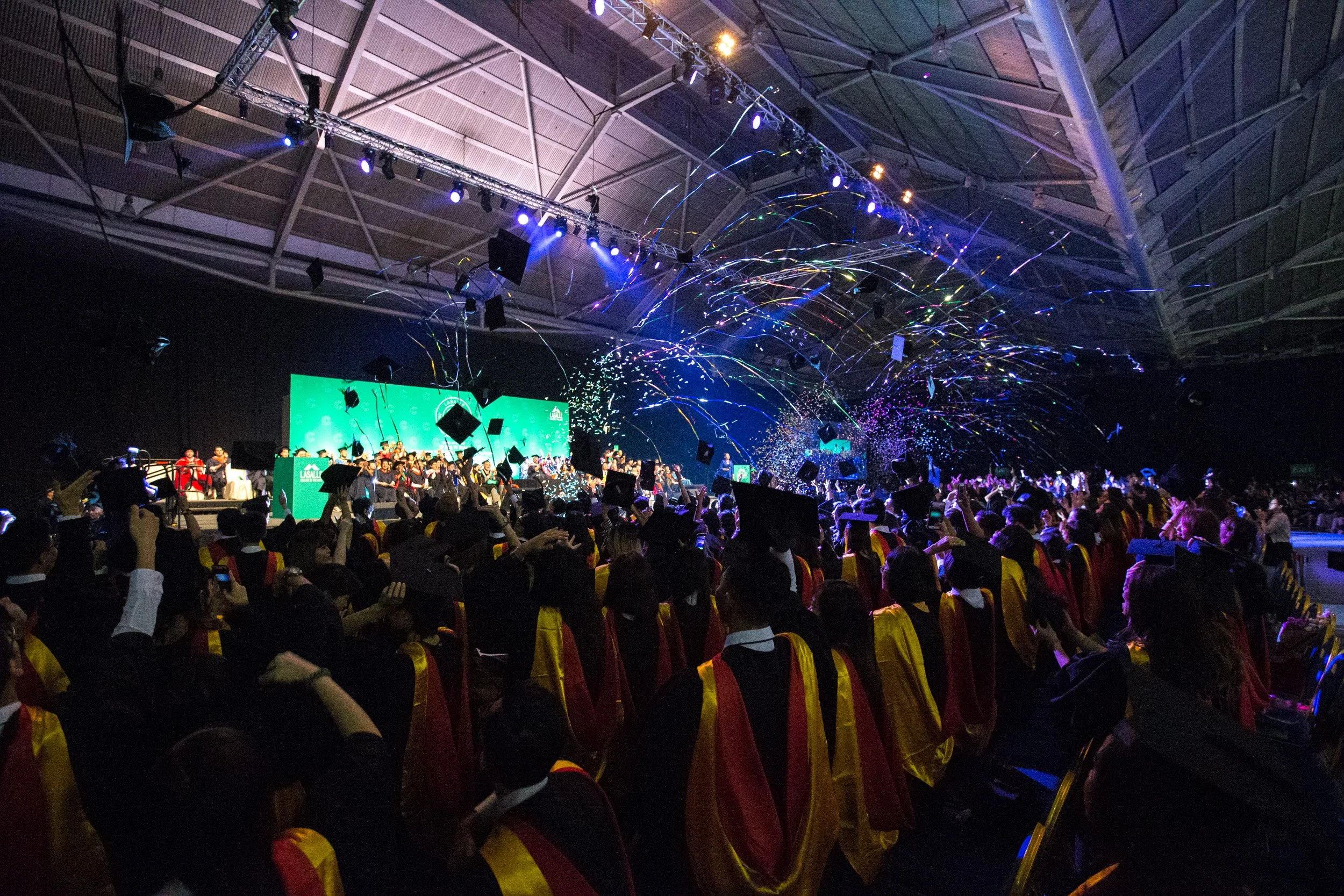  Wide action shot of graduating students throwing their graduation caps into the air in celebration. 