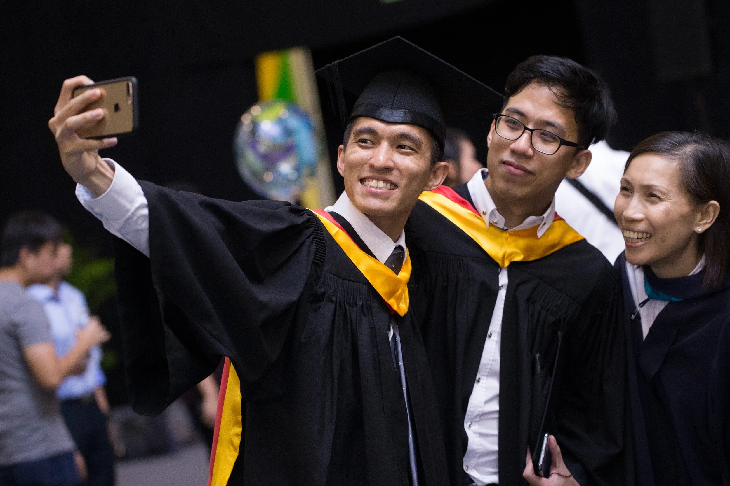  Male graduate taking celebratory photos with peer friends in the exhibition hall foyer. 