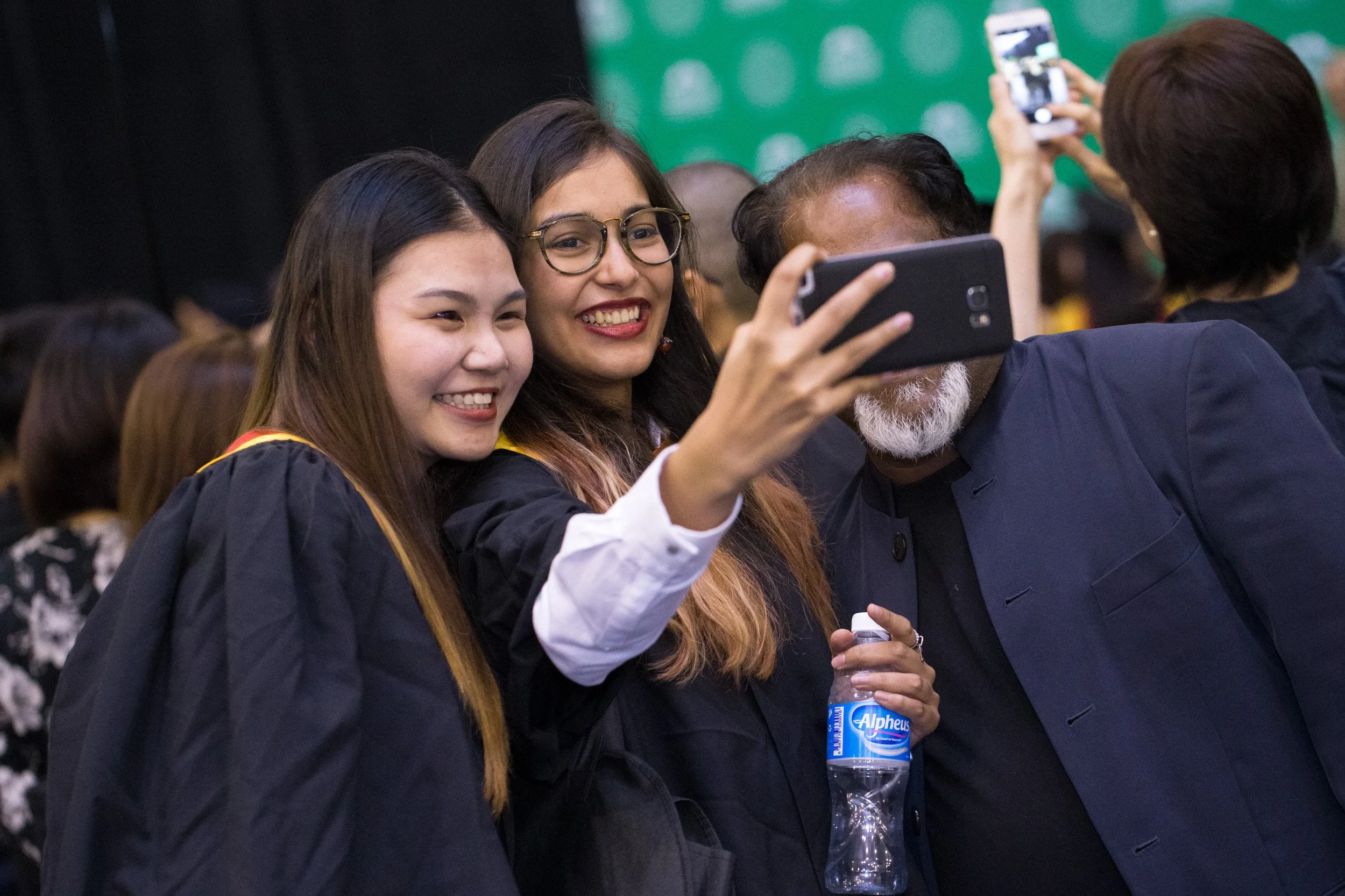  Three female graduates wearing academic gowns posing together for a commemorative photo. 