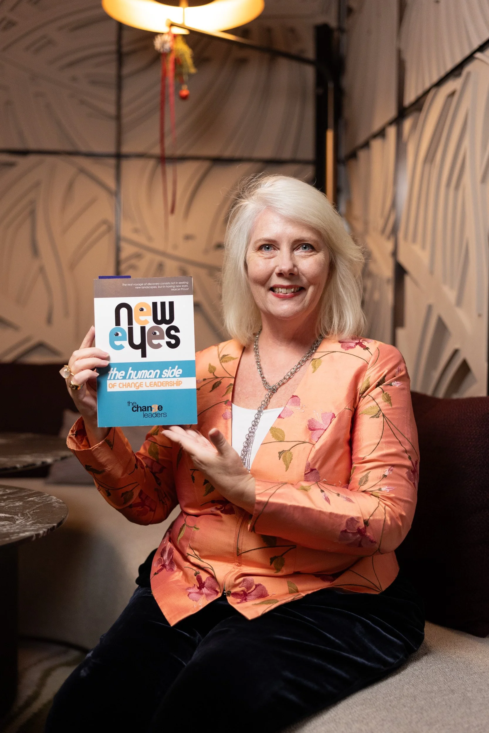 Author Joanne Flinn holding a copy of New Eyes: The Human Side of Change Leadership at PLUME Singapore.
