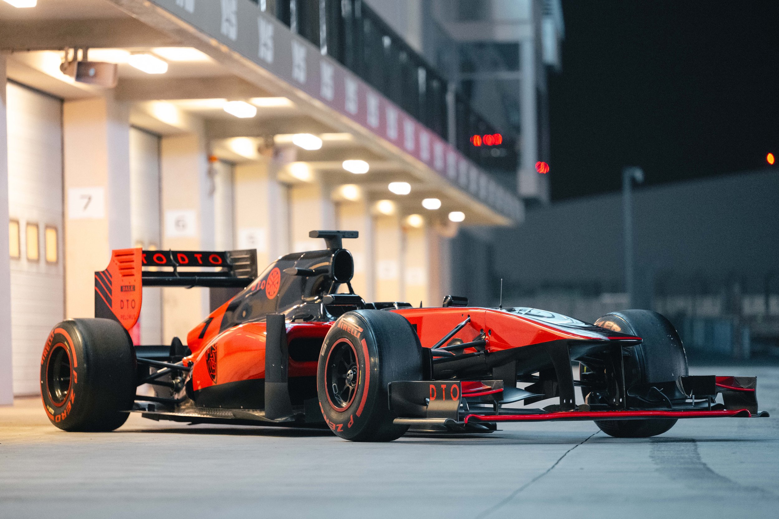 A red and black Formula 1 race car parked in a race track garage at night.