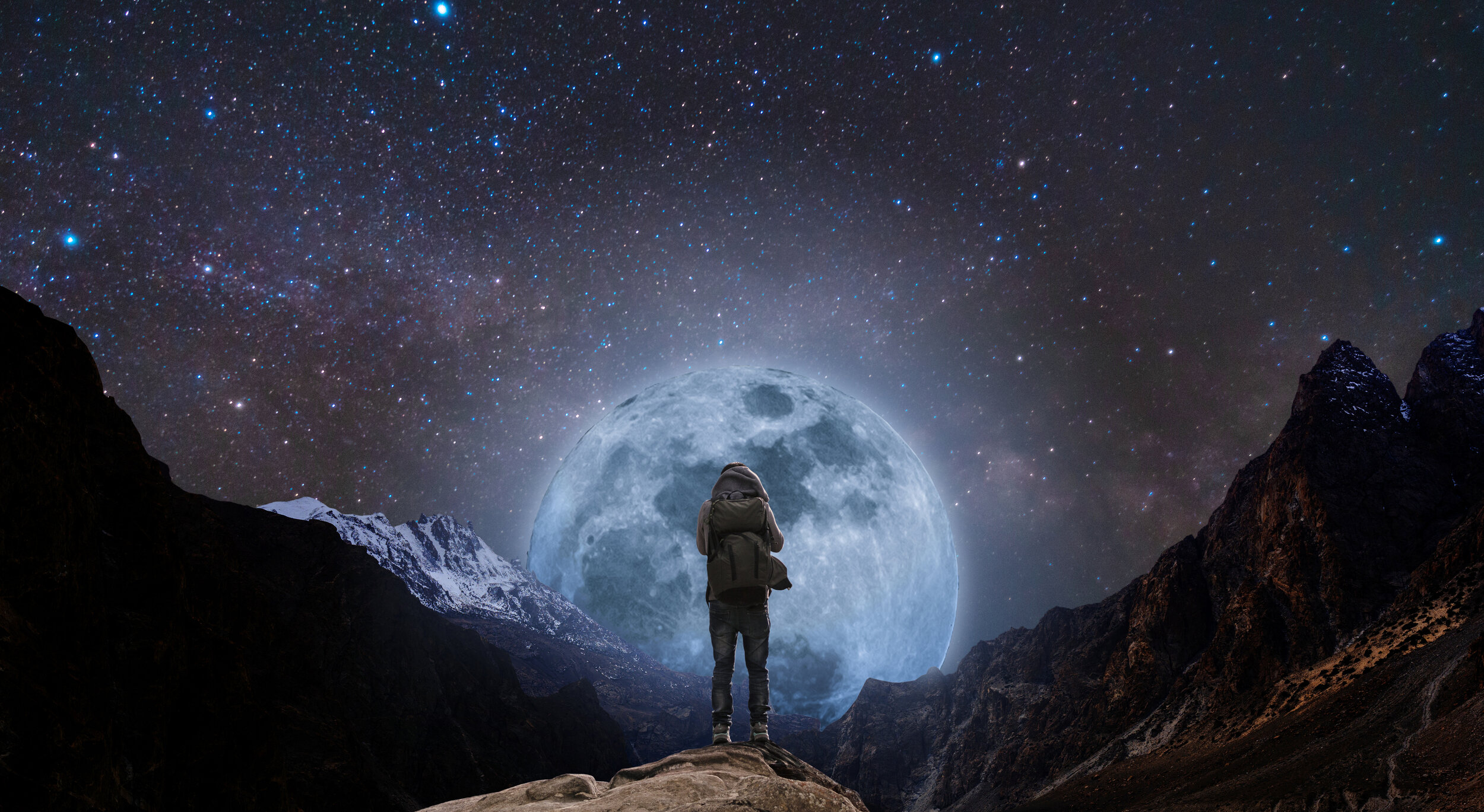 a-man-with-backpack-standing-on-mountain-peak-at-night,-and-silhouette-mountain-with-bright-full-moon-and-sky-full-of-stars-971852206_4268x2337.jpeg
