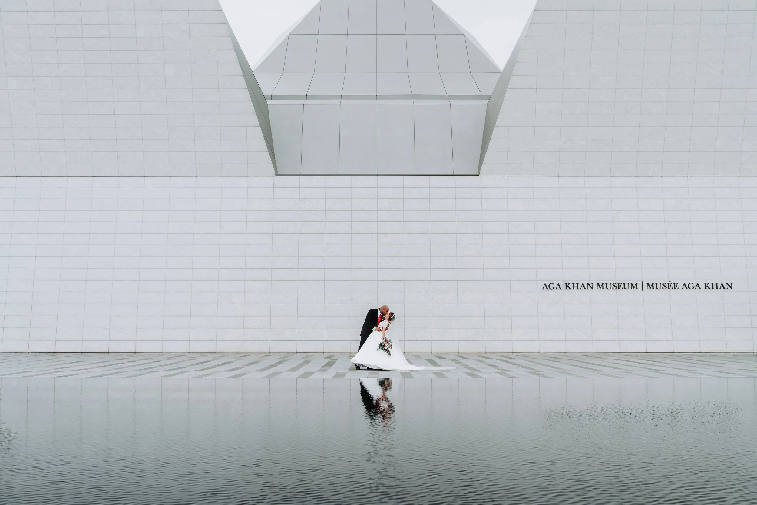 A bride & groom enjoy their wedding at the Aga Khan Museum, Toronto, with their reflection visible in a pool of water captured by documentary wedding photographer, Maple & Clover 