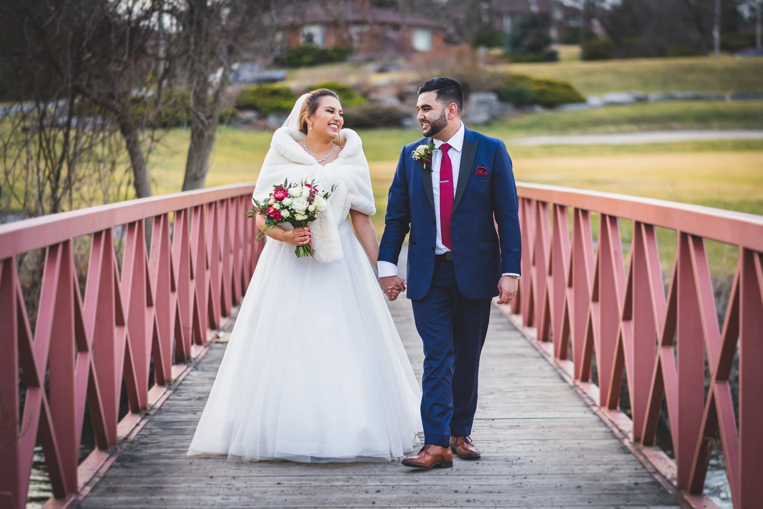 A bride & groom walk over a bridge hand in hand, in Ontario, captured by documentary wedding photographer, Maple & C lover.