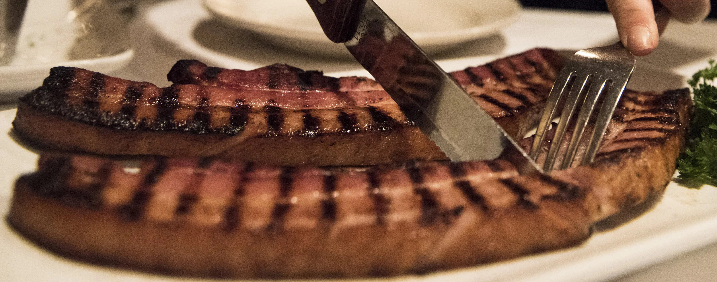 UpcloseImageOfCookedThickCutBaconWithForkAndKnifeCuttingIntoIt.jpg