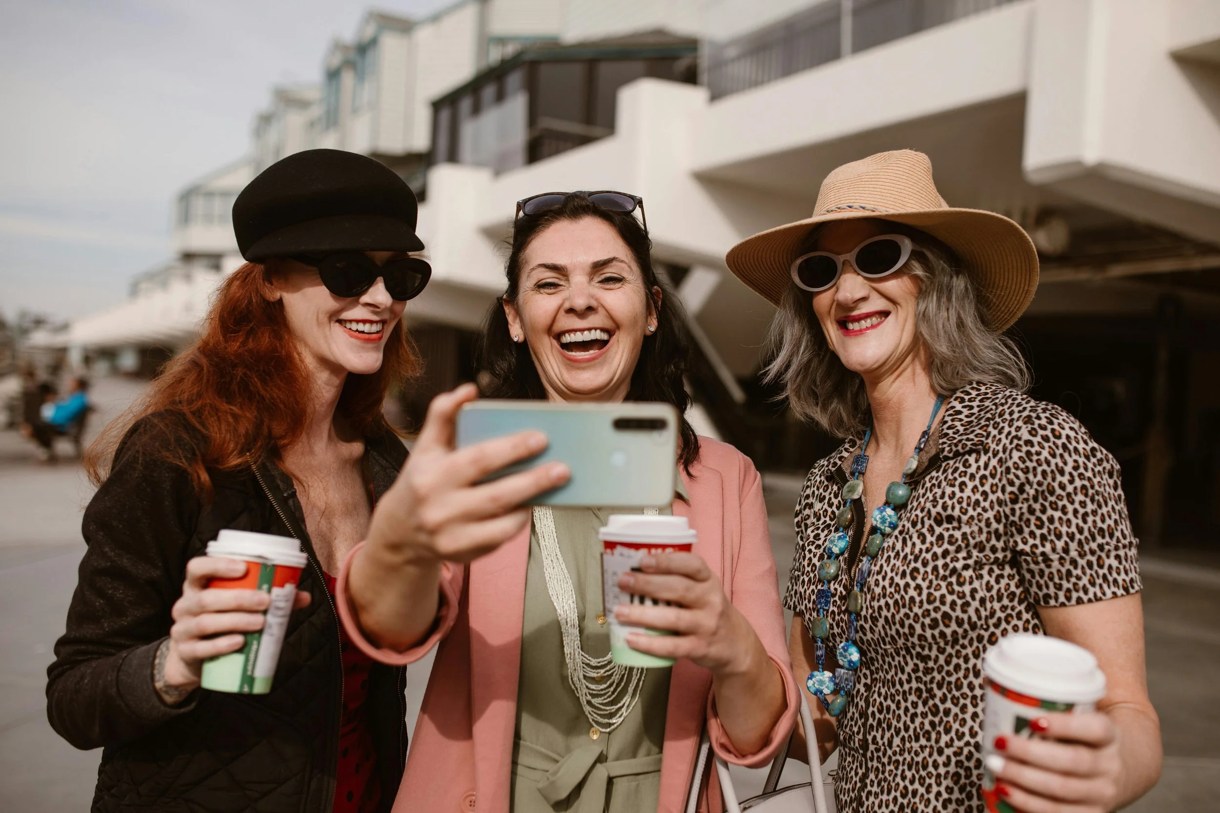 three midife women smiling with coffee and taking a selfie
