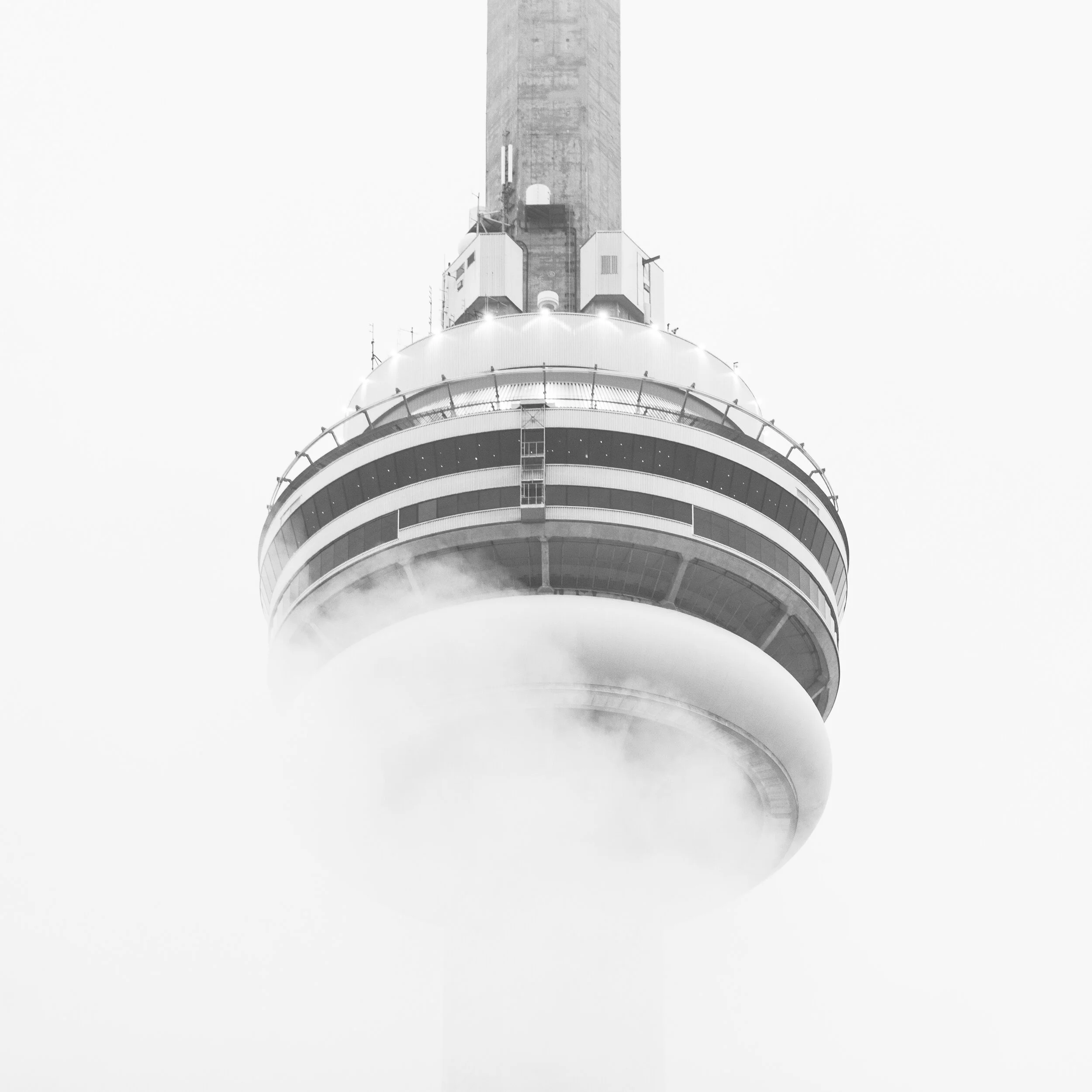 Close-up of a tower with a circular observation deck at the top, featuring glass windows and metallic railing, with the upper part of the tower visible against a plain, overcast sky.