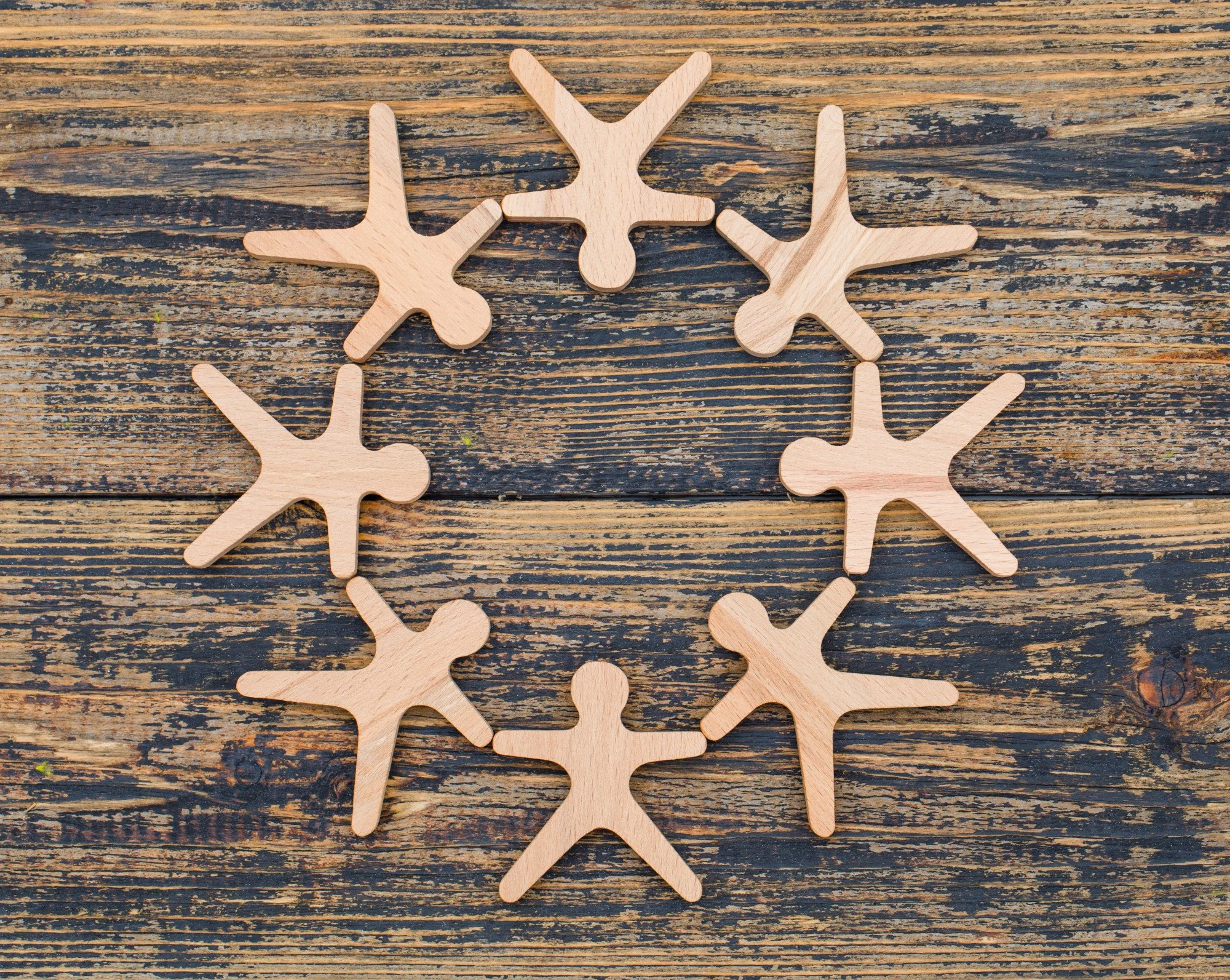 Eight wooden cutouts of people, arranged in a circle on top of a wooden surface