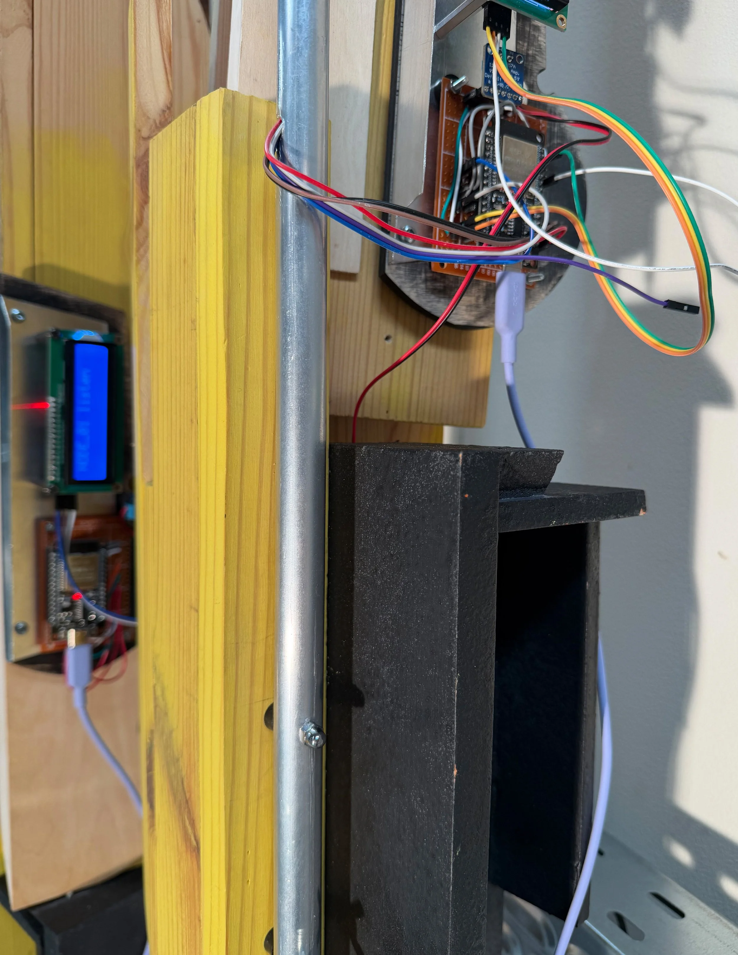 Echoic Recursion, detail — ESP32 microcontroller and coloured wiring exposed behind yellow pine element, black speaker housing and blue LCD display visible, deliberate infrastructure as material