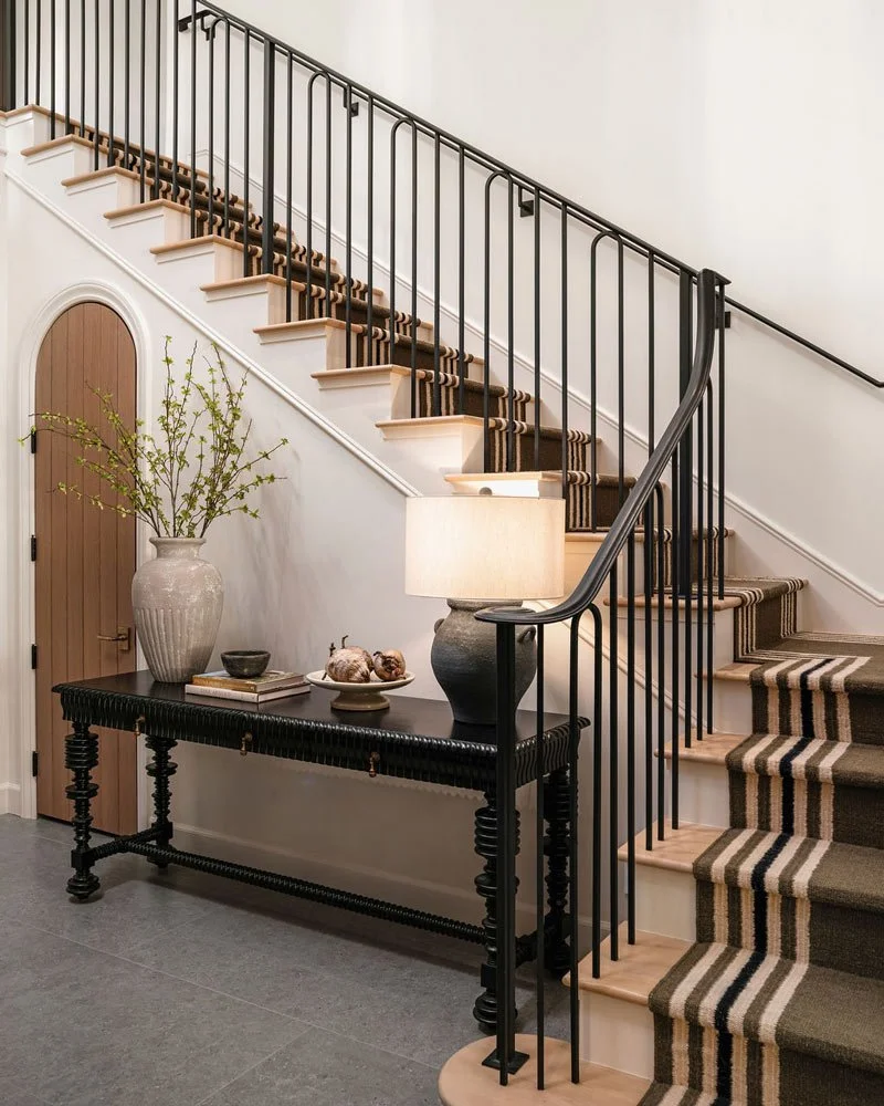 Indoor staircase with black metal railing, wooden steps with striped carpet runner