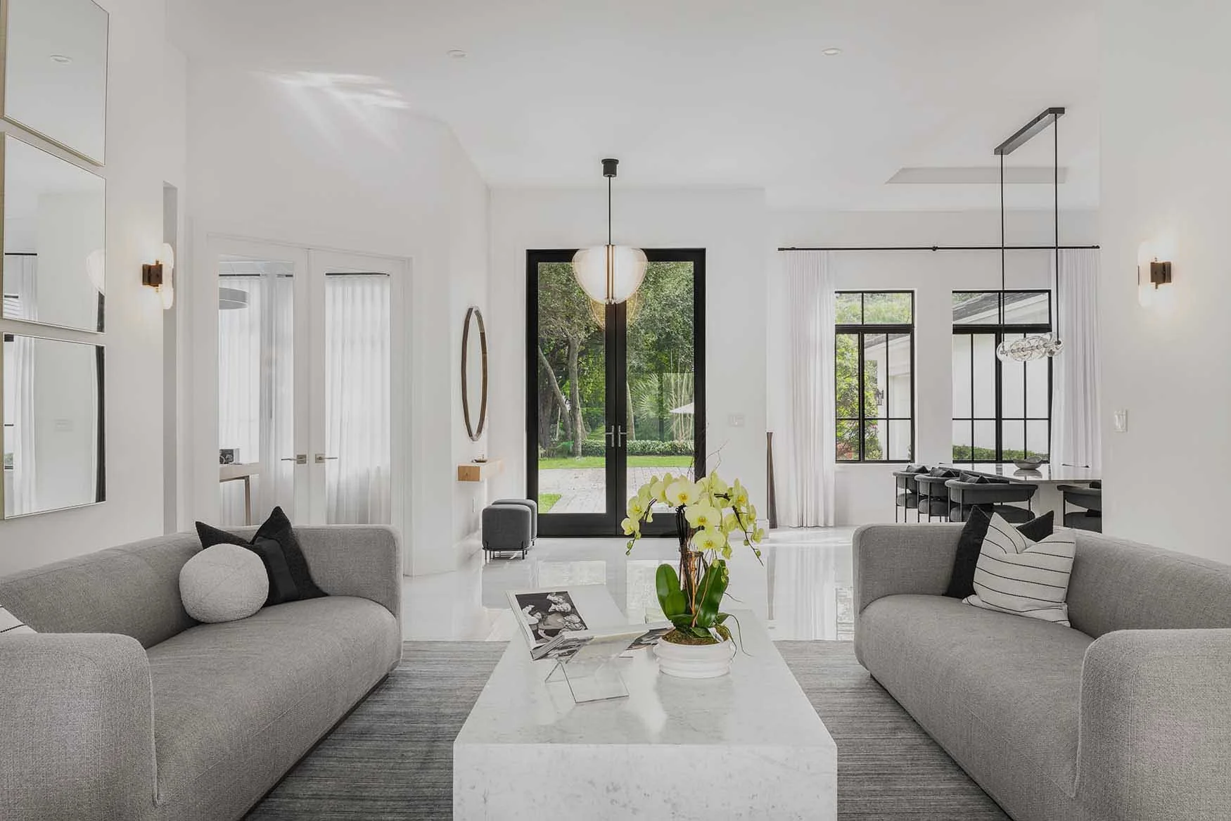 Contemporary living space with gray couches, overlooking a modern entryway in a residence designed by CURATED. in Pinecrest