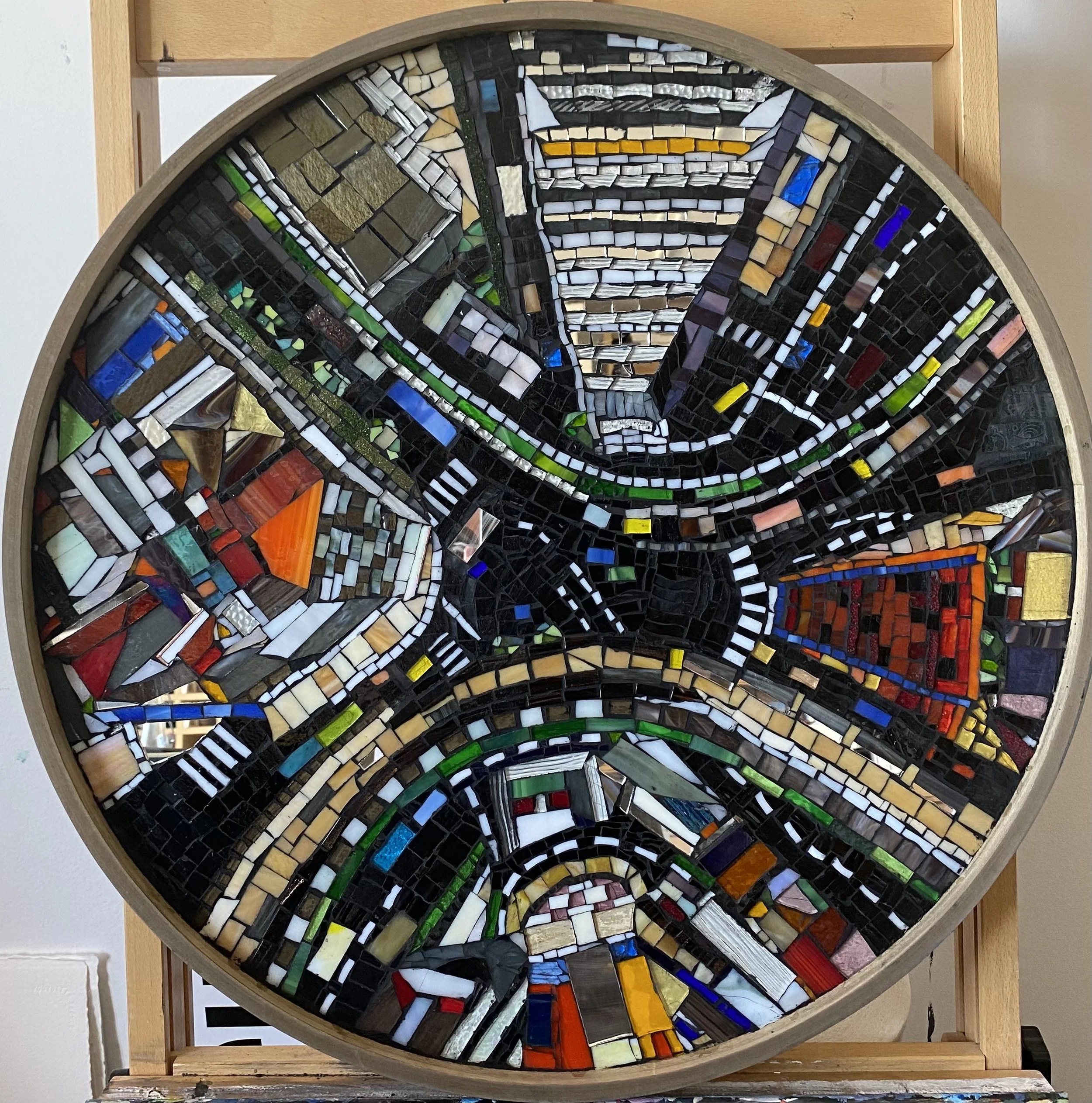 Round mosaic artwork with various colored glass pieces arranged in abstract patterns.