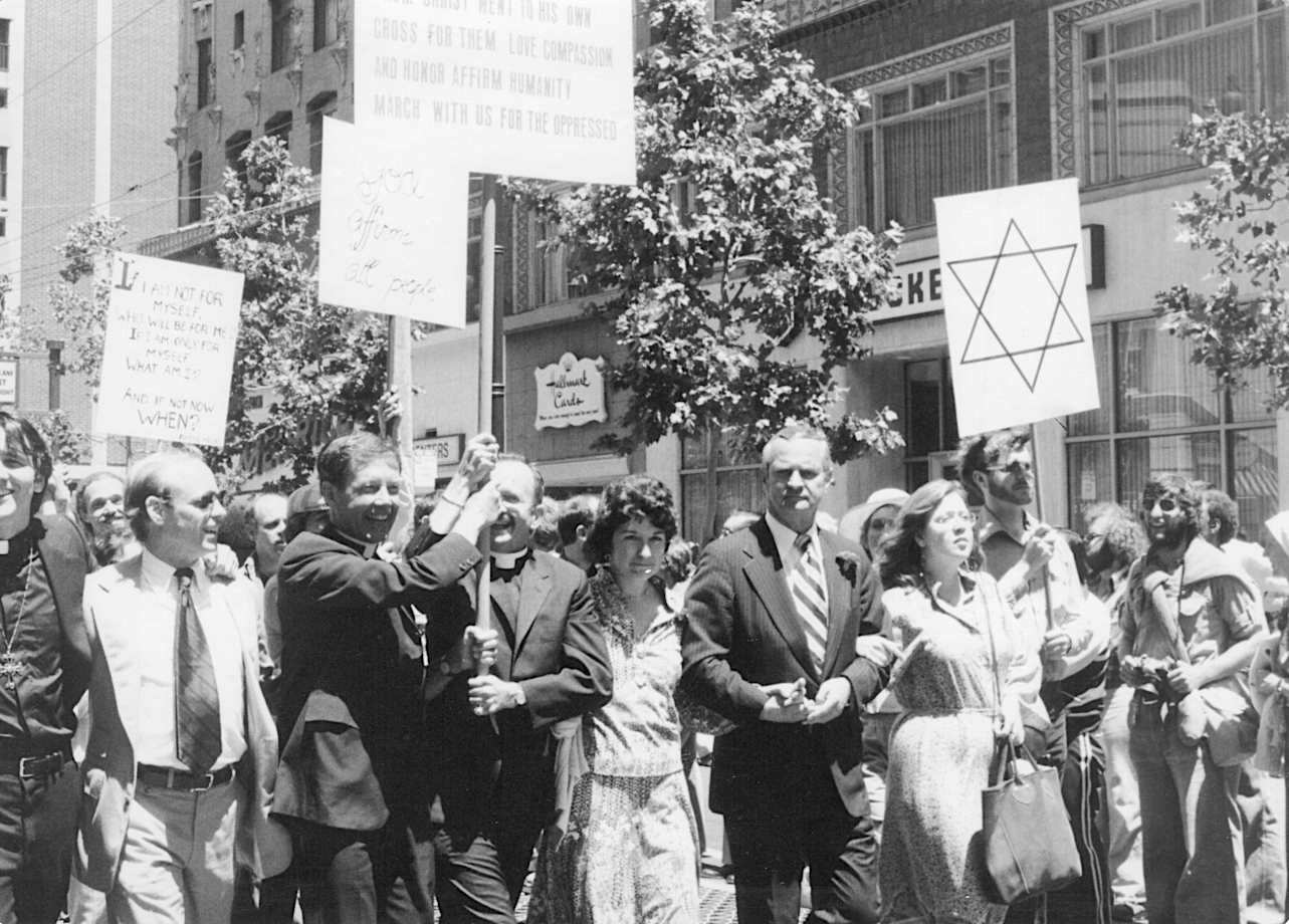  Group of people, including priests, holding a sign that reads "God affirms all people" and another of the Star of David, 1978;  photograph by Elaine Gay Jarvis, Elaine Gay Jarvis Papers (2018-90), GLBT Historical Society. 