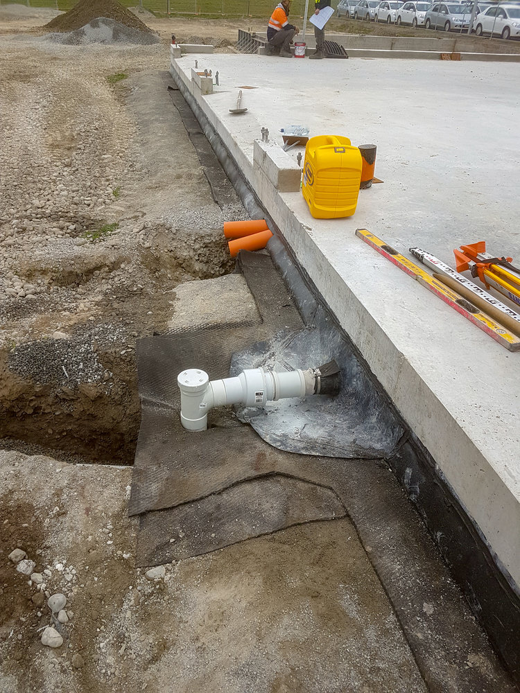  Exterior sewer drain installed on the side of a concrete slab with the blue and black Hannon Civil logo in the corner of the image with the Rangiora sign in the distance 