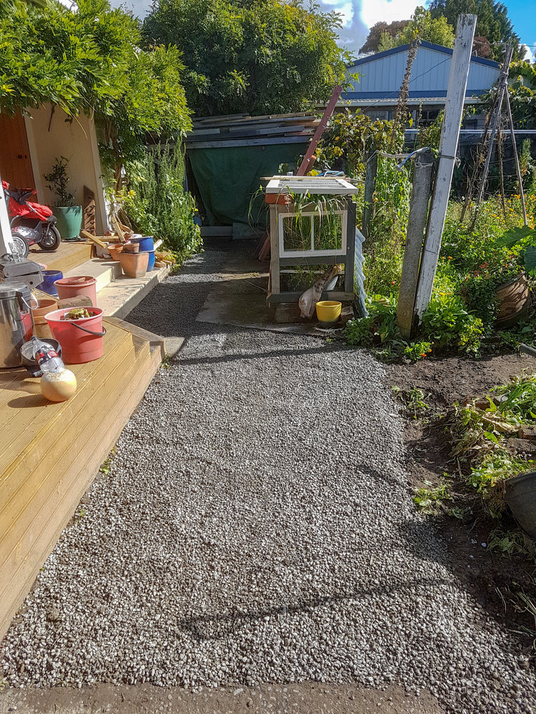  A garden gravel path newly installed with a fresh golden wood decking area. Landscaping equipment, a wheelbarrow and other landscaping and ground works tools organised on the deck 