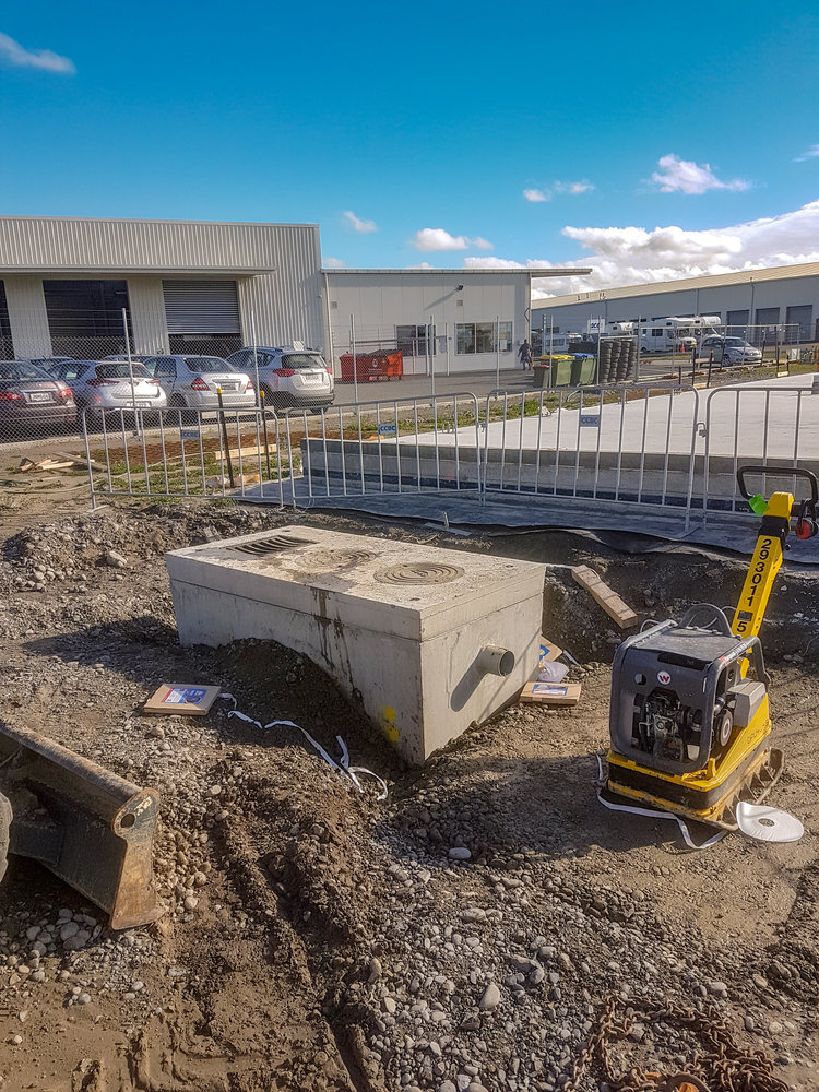  A fenced off area on a construction site with a plate compactor and a newly installed sewer system with the Christchurch City Airport building in the background 