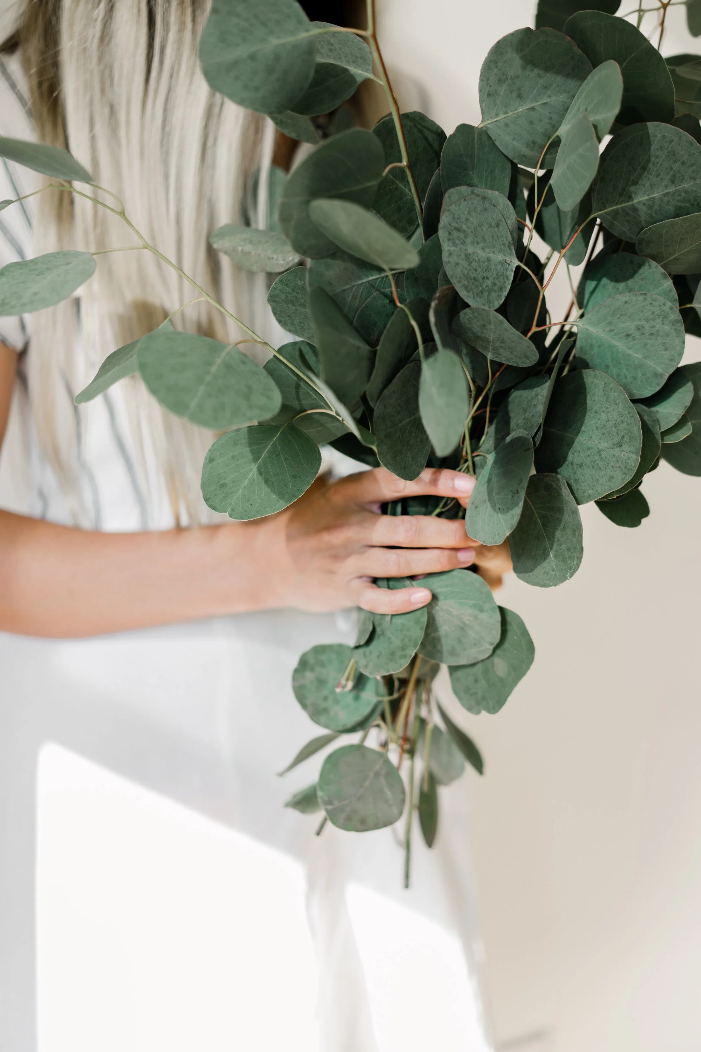 Woman holding a bundle of fresh eucalyptus stems against her clothing
