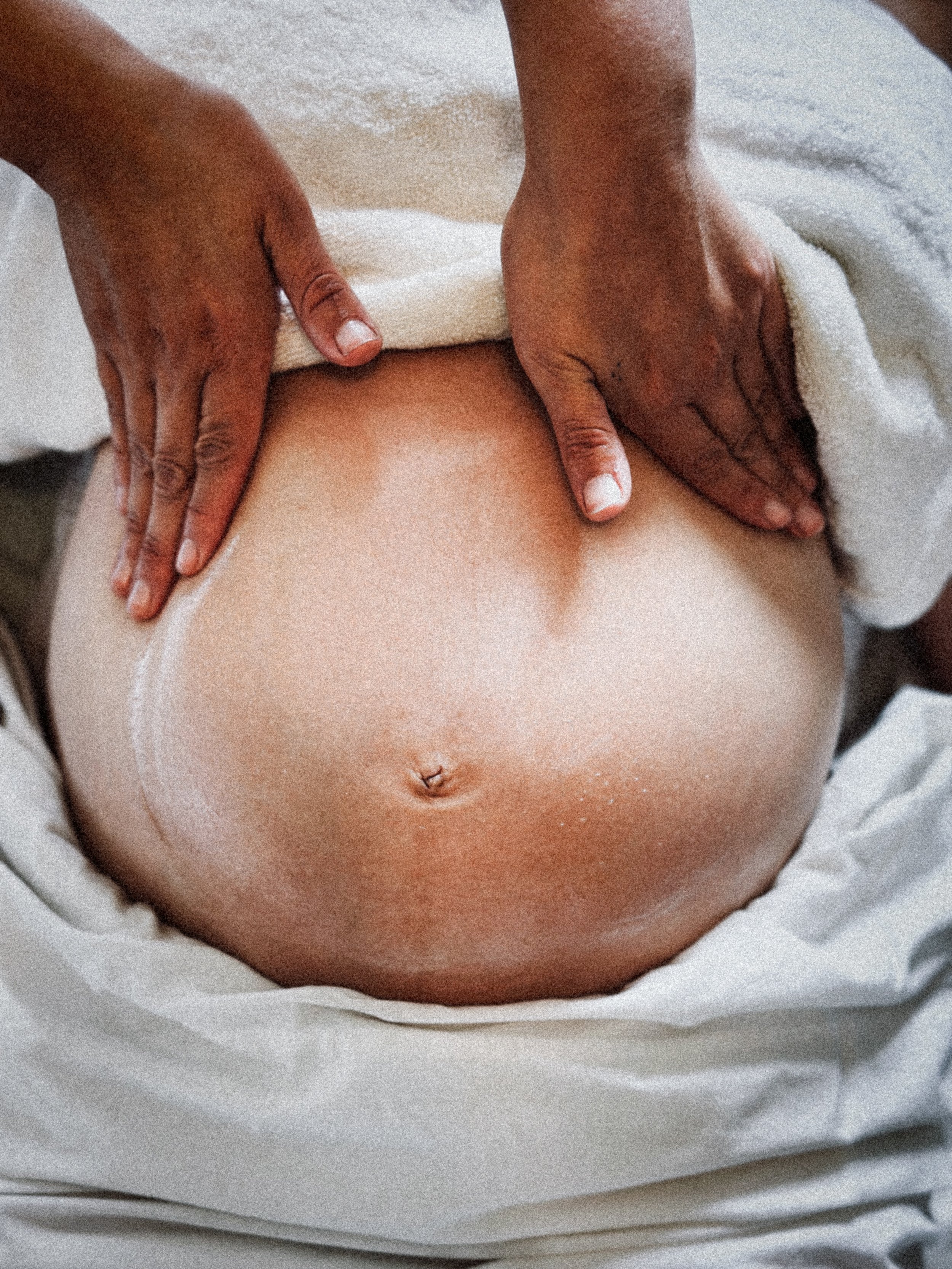 Pregnant round belly close up with and acupuncturists hands massaging the belly to represent labor induction 