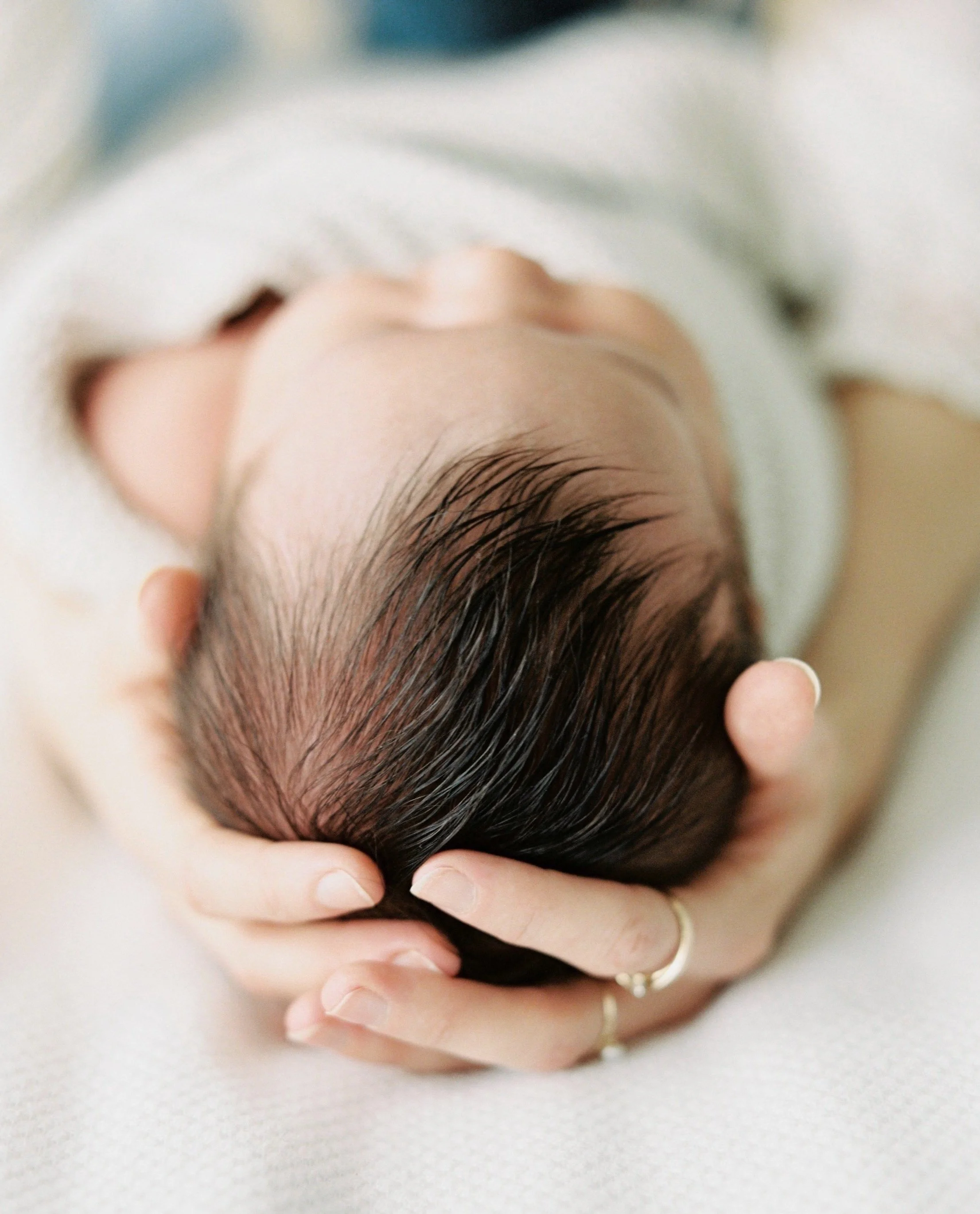 close-up of a newborn baby's head with a lot of dark hair and the mom is cradling the baby's head in her hands to represent acupuncture for labor induction
