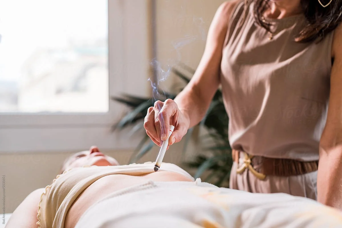 a fertility acupuncturist in a brown dress with a brown belt performs moxibustion on the abdomen of a woman who is using fertility acupuncture to support IVF