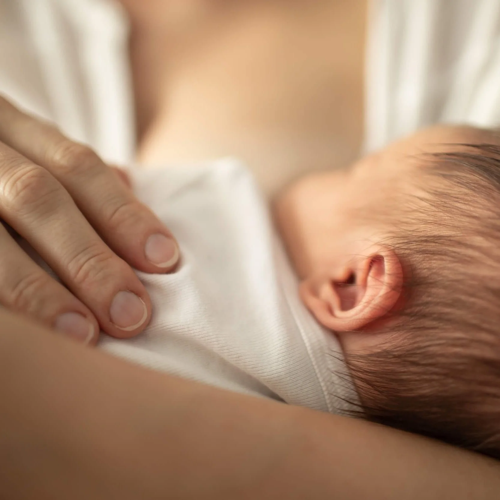 Newborn baby resting against their mother's chest with her hand gently placed beside them