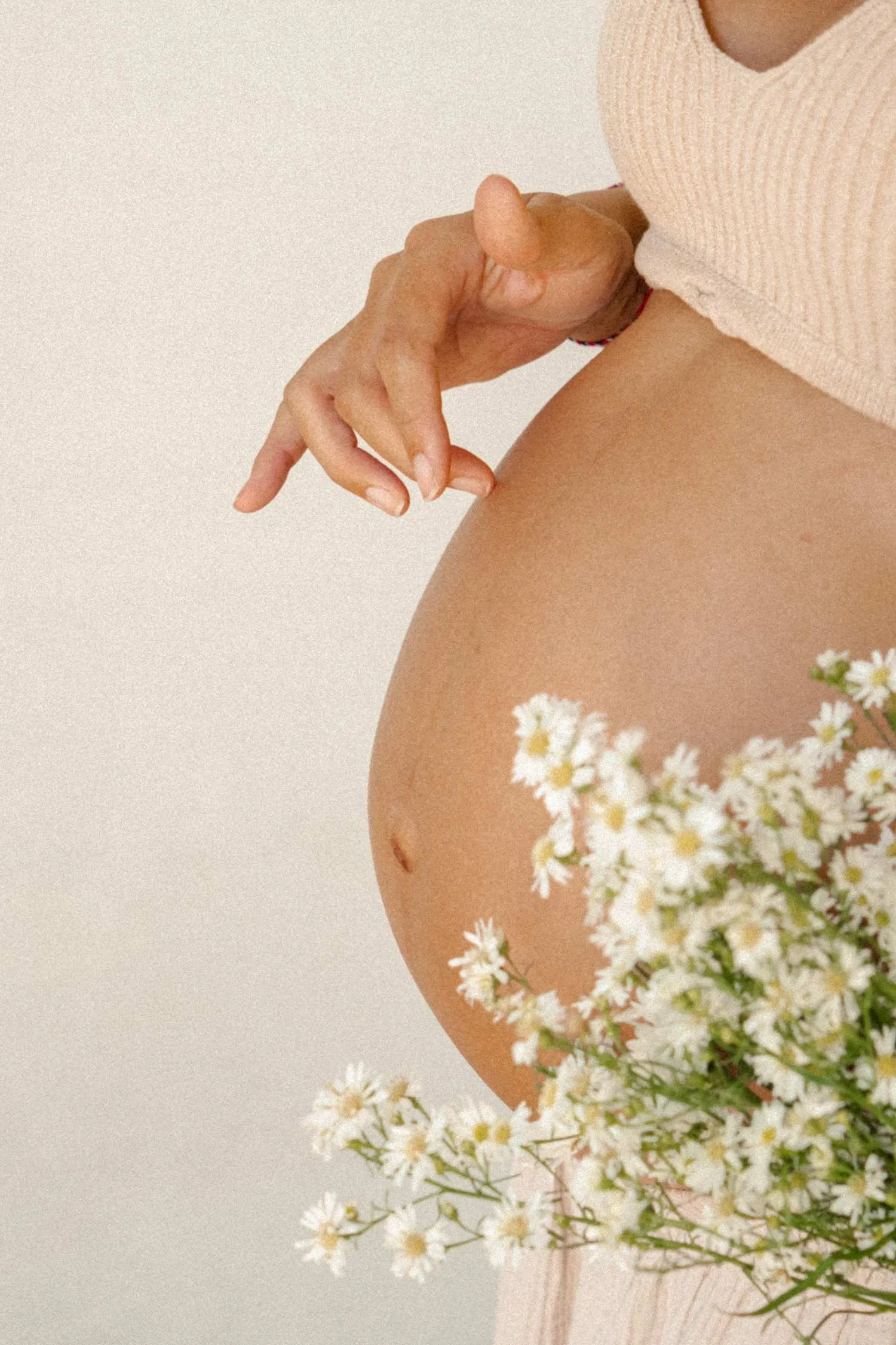 Pregnant belly and hand holding a bouquet of white daisies