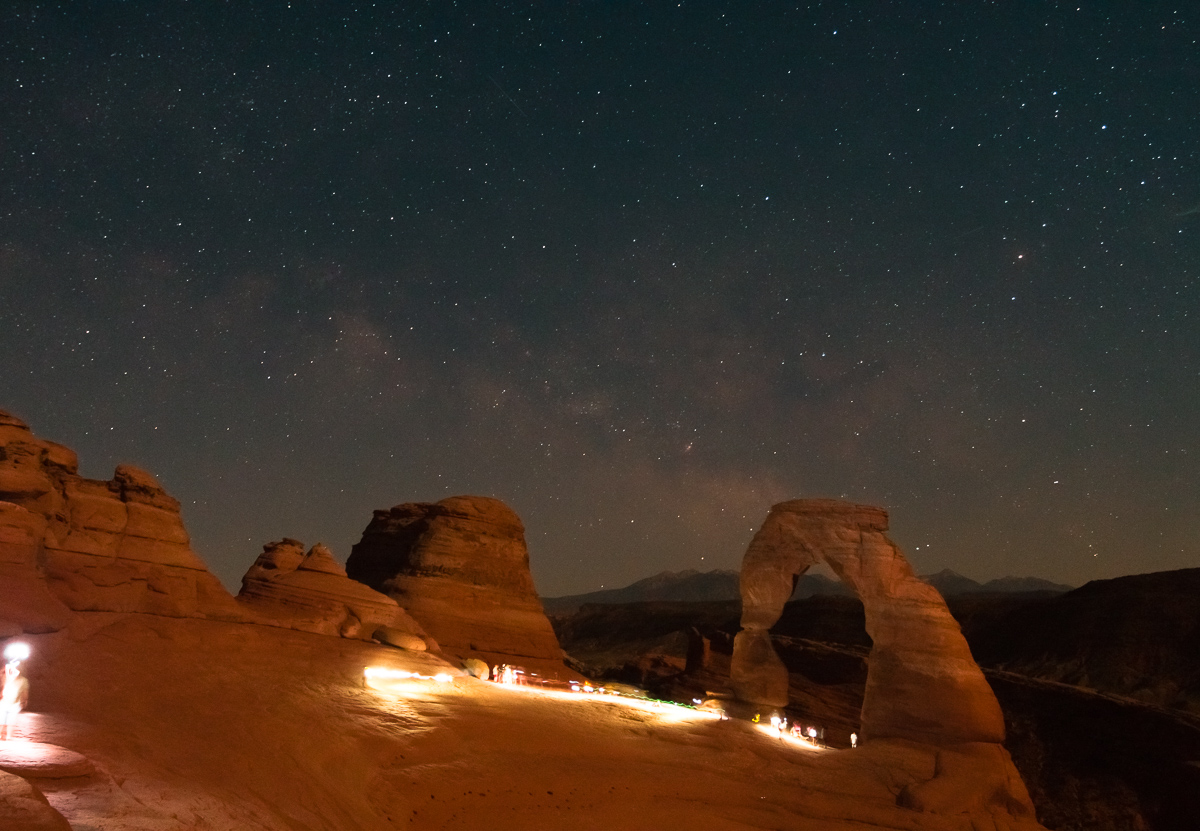 Hikers Illuminate Delicate Arch as the Milky Way rises