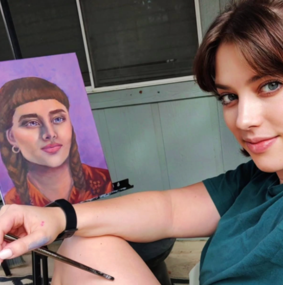 The artist, Morgan McVay, next to a portrait painting she's painting on an easel.