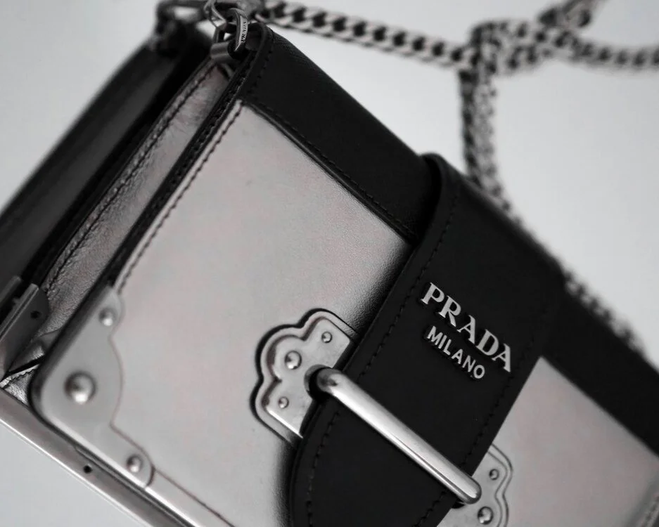 Nærbilde av en svart og sølvfarget Prada veske med kjedestropp.