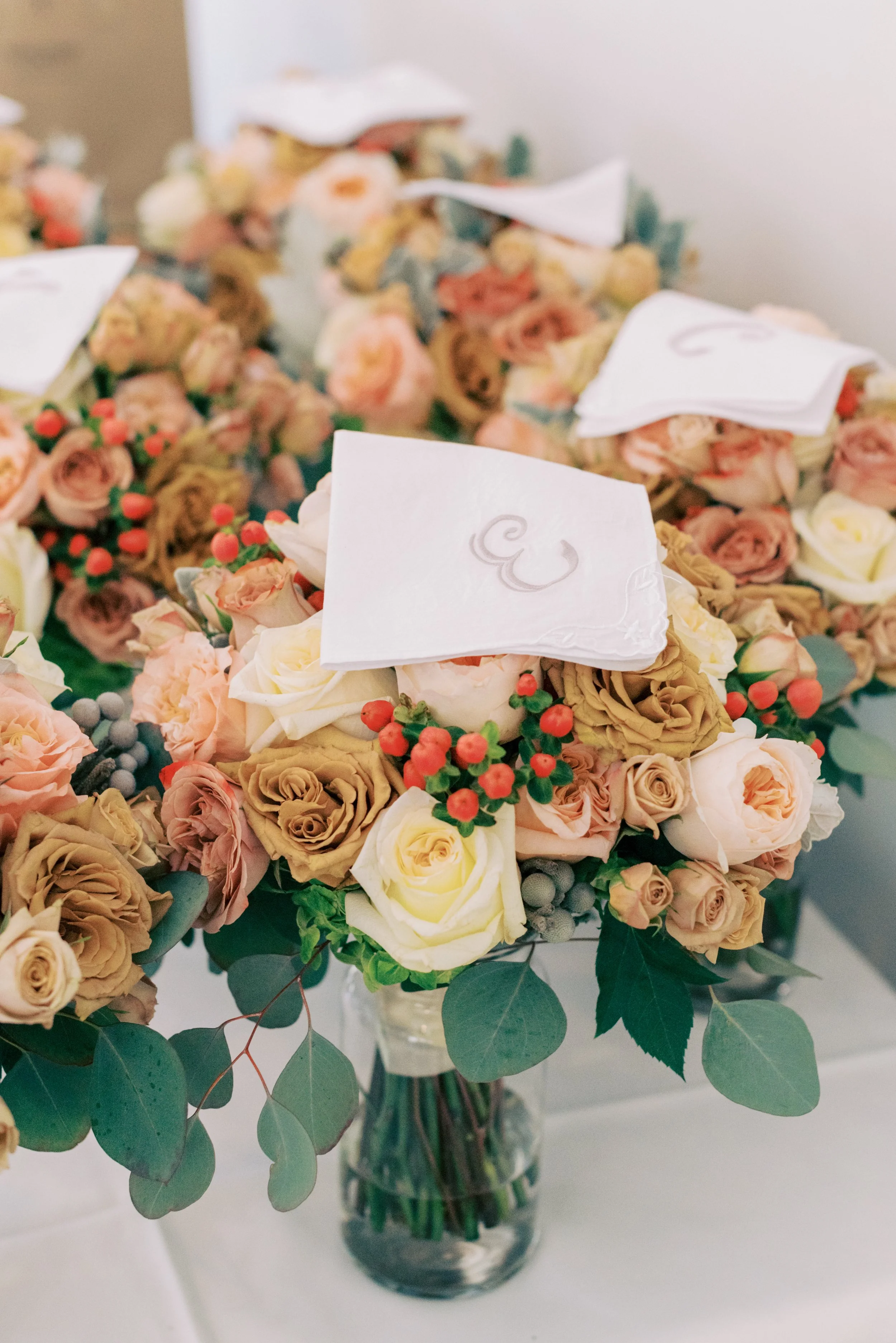 A bouquet of pink, cream, and brown roses with green leaves in a glass vase.