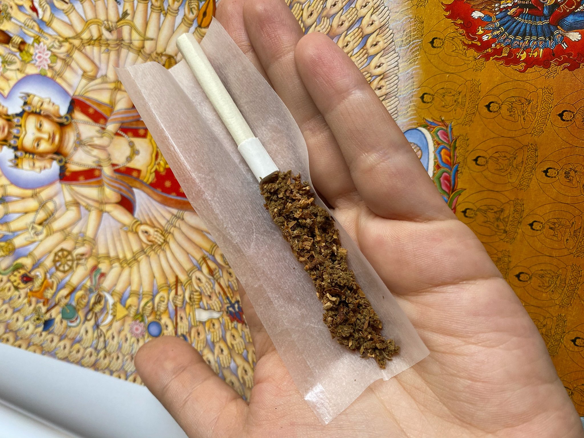 Mão segurando beck de tabaco com haxixe, com piteira longa e fundo com estampa indiana