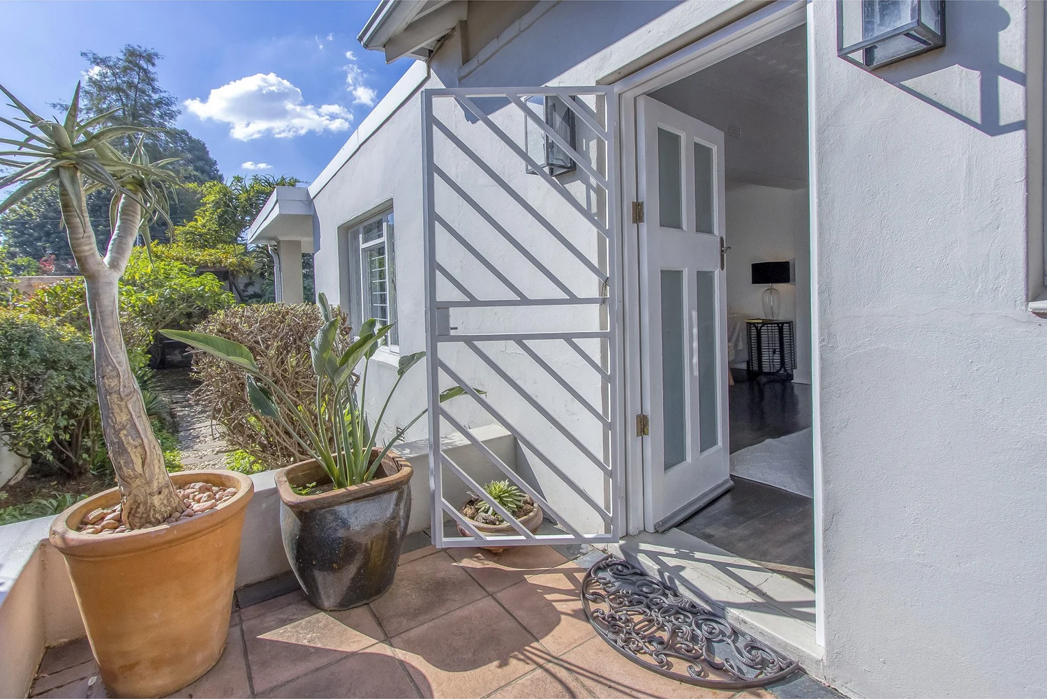 Sunny front entrance with potted aloe and security gate